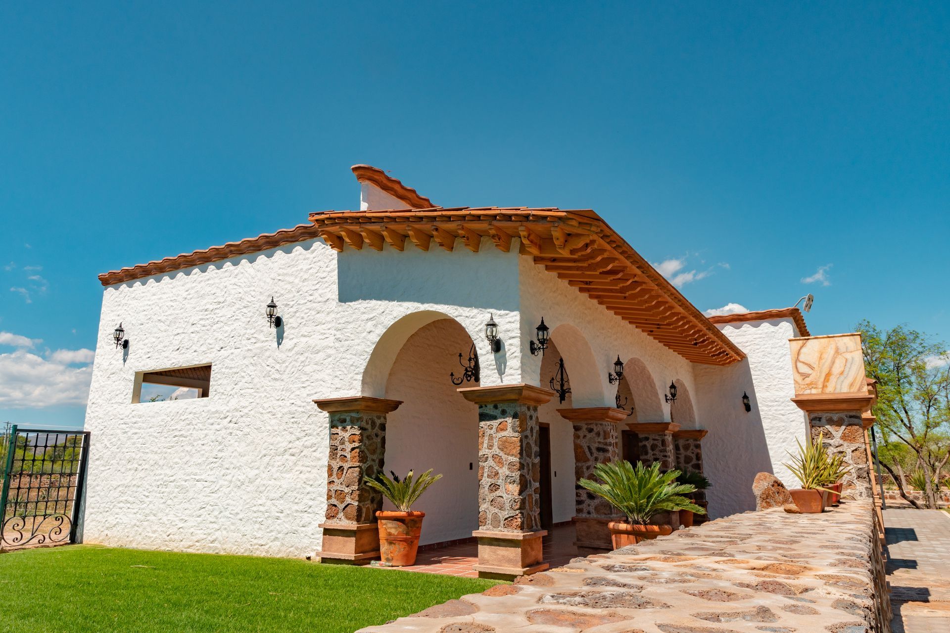 White stucco building with arched entry, brown pillars, and tile roof against a blue sky.