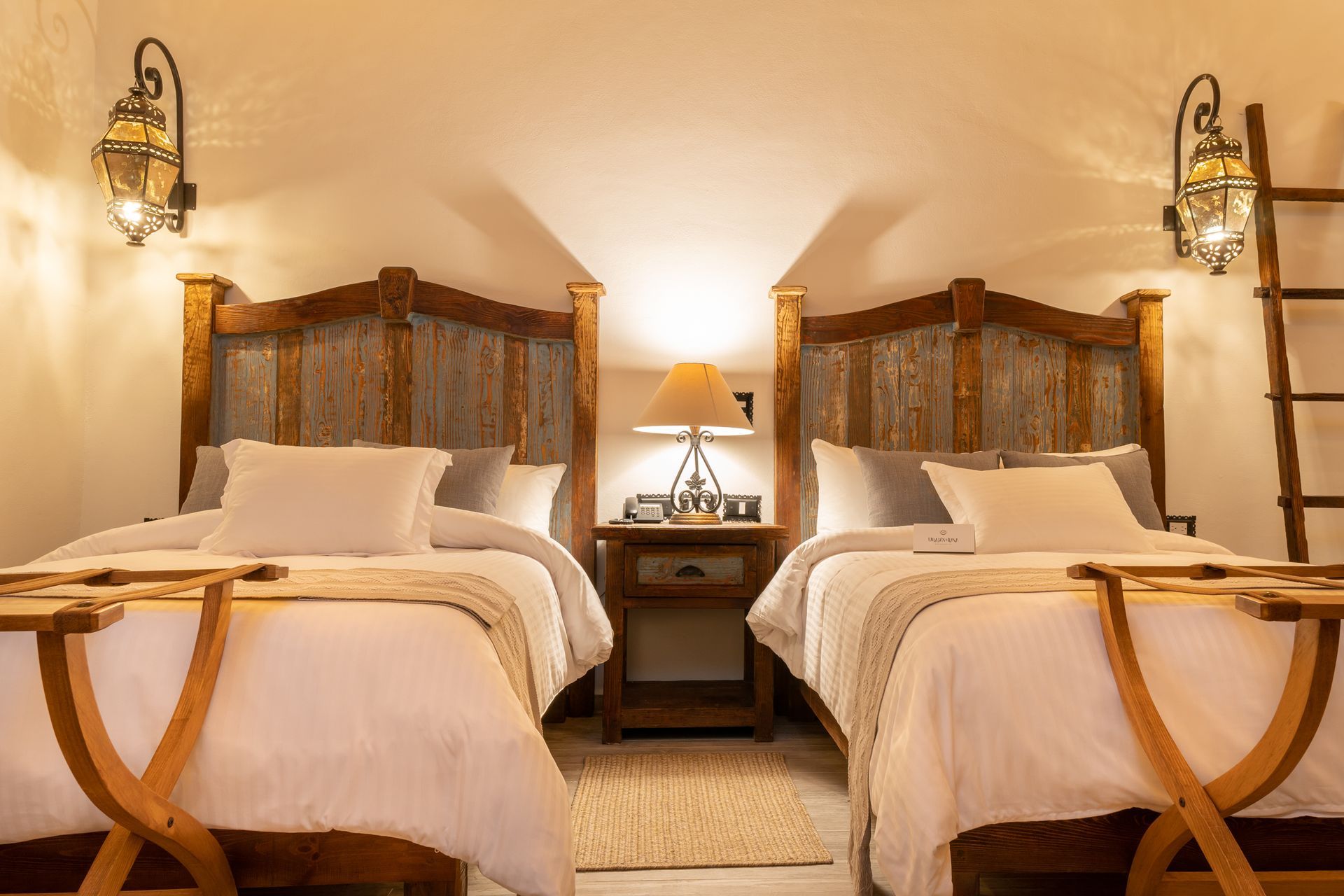 Two twin beds in a room with wooden headboards, bedside table, and sconce lighting.