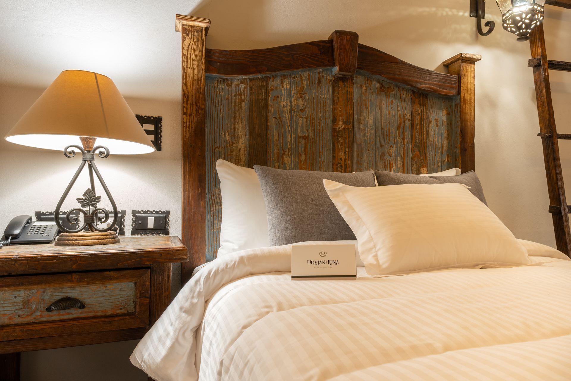 Bedroom with rustic wood headboard, bedside table with lamp, and ladder.