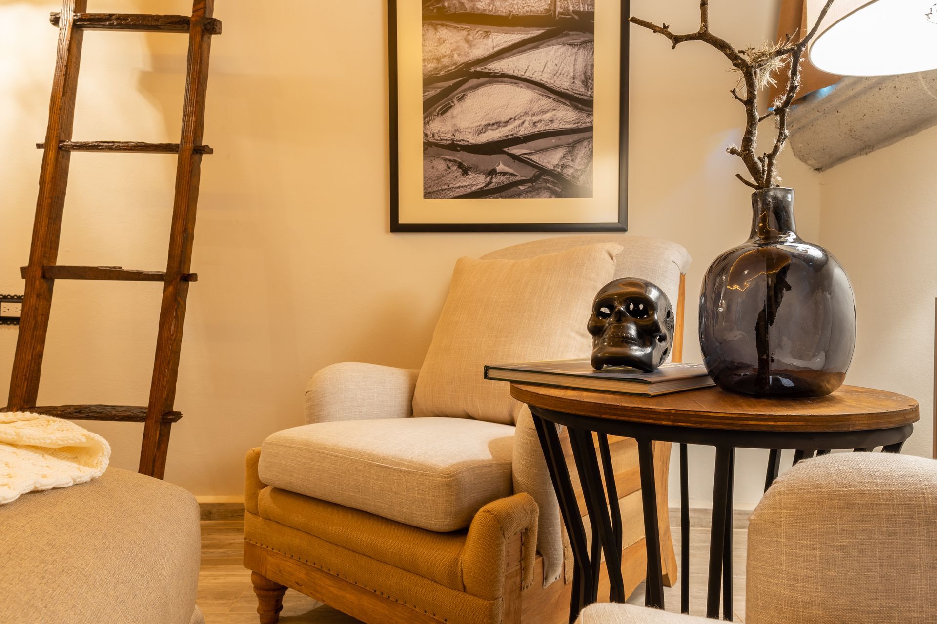 Cozy reading nook with a chair, side table, decor, and wooden ladder against a light-colored wall.