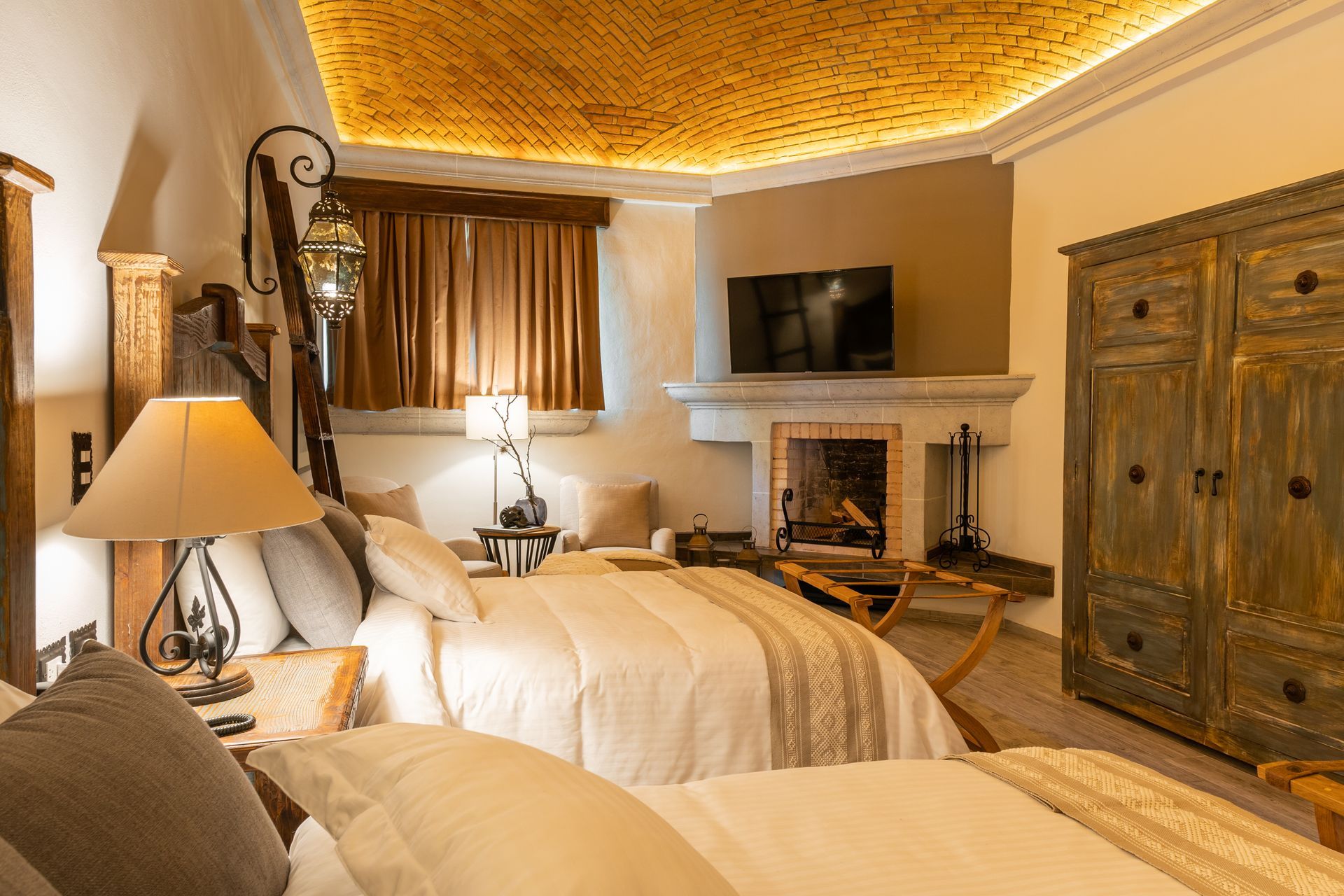 Cozy hotel room with two beds, fireplace, antique wardrobe, and ornate ceiling.