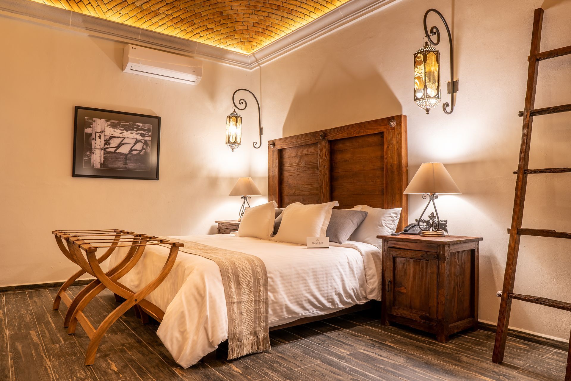 Bedroom with wooden bed, bedside table, lamps, and decorative lanterns. A luggage rack sits at the foot of the bed.