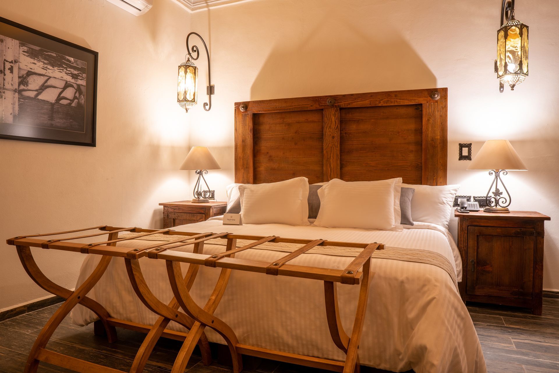 Bedroom with a large wooden headboard, two nightstands with lamps, and a luggage rack.