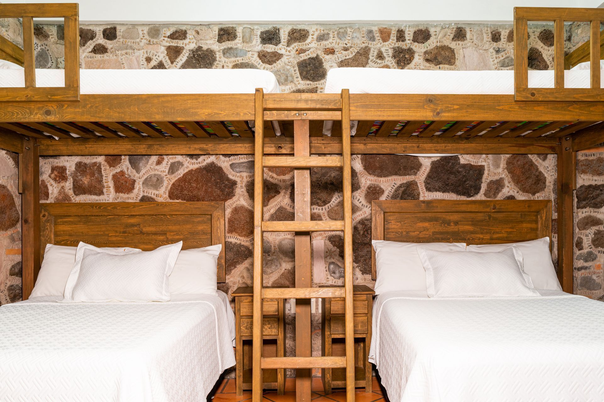 Two bunk beds with double beds, wood frame, stone wall background.