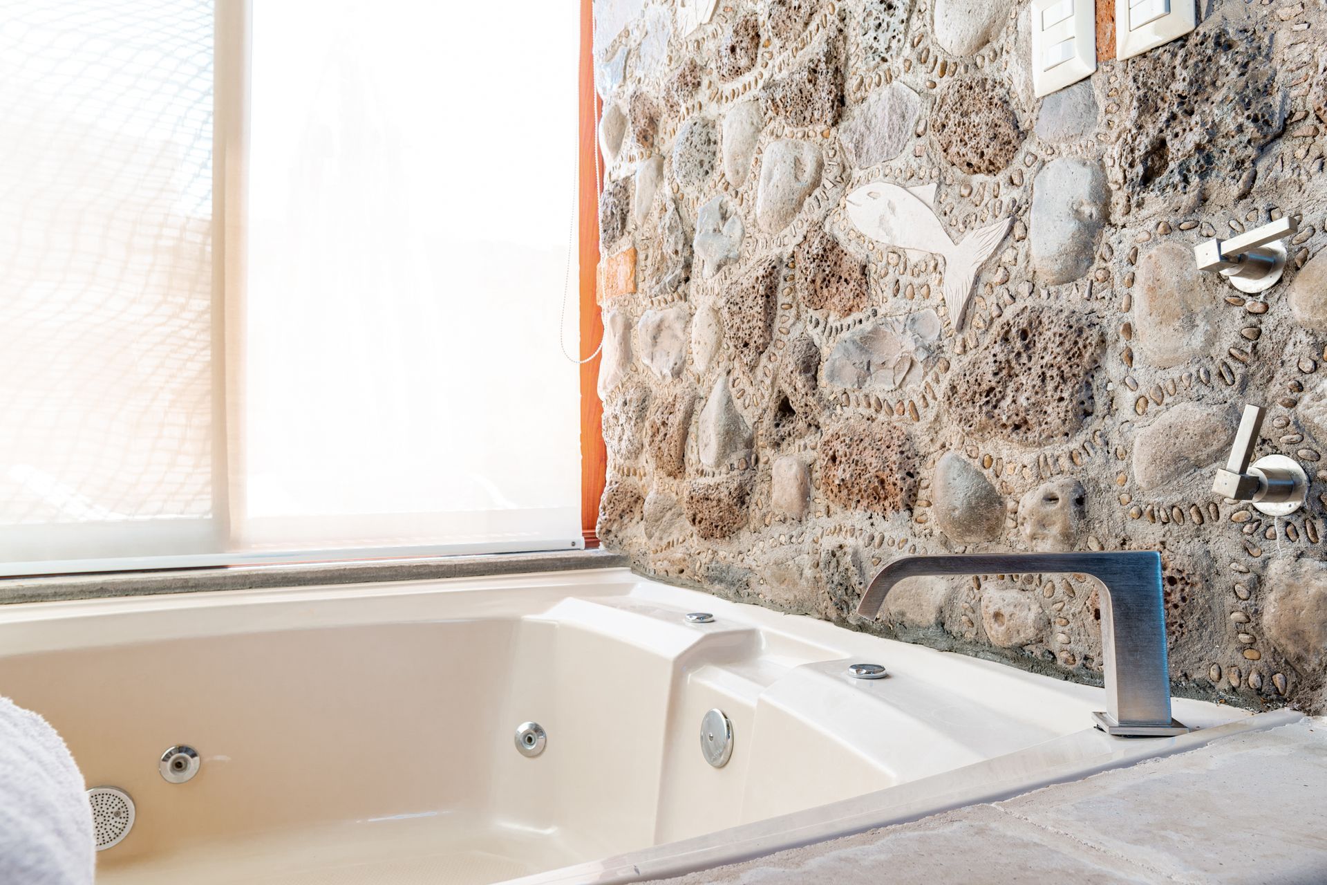Jacuzzi tub next to a window and stone wall; chrome faucet and fixtures.