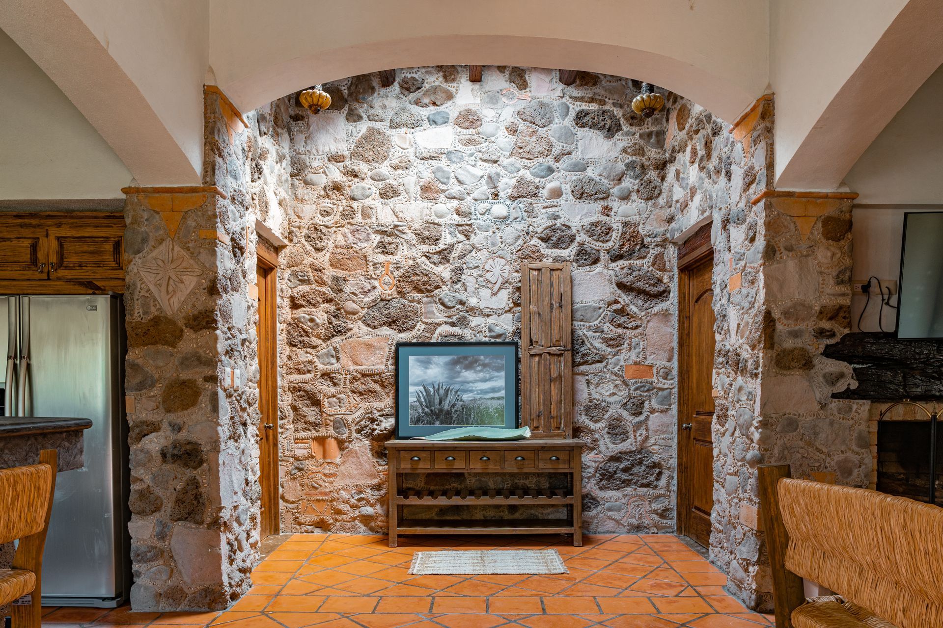 Interior of a room with stone walls, terracotta floor, wooden doors, and a cabinet with a framed picture.