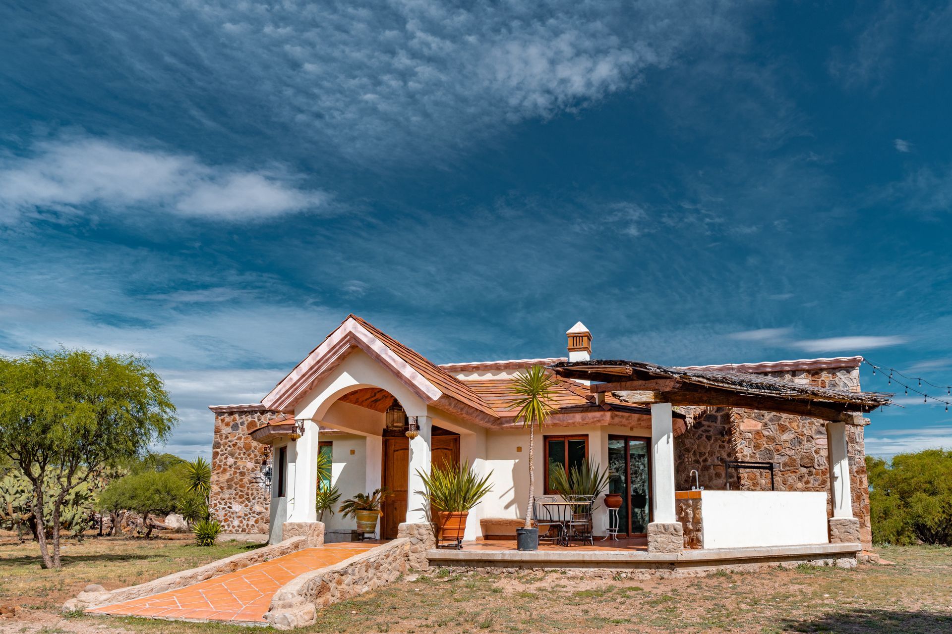 A white adobe house with stone accents, terra cotta walkway, and blue sky background.