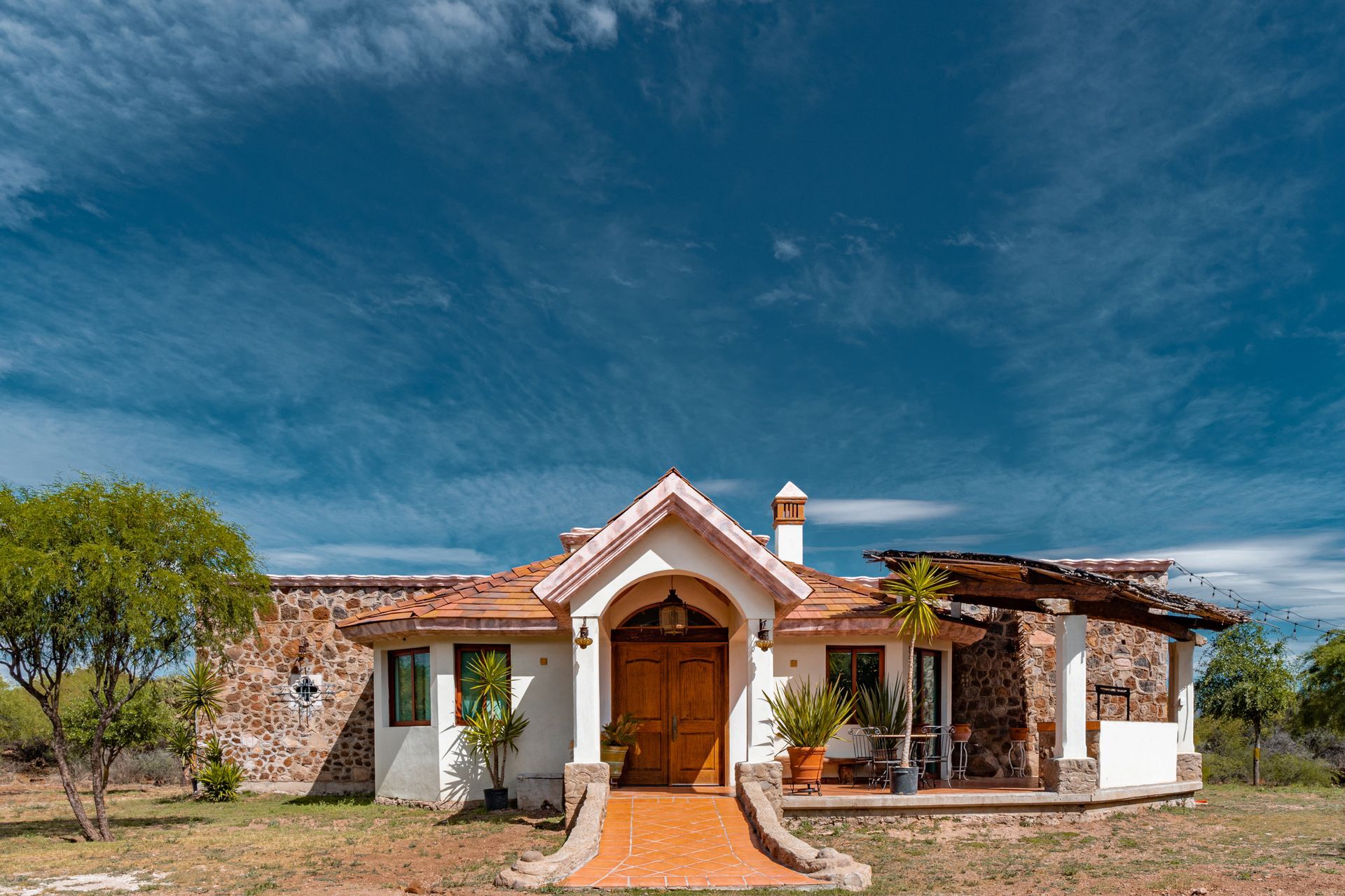 Stone and stucco house with terracotta roof, set against a blue sky with wispy clouds.