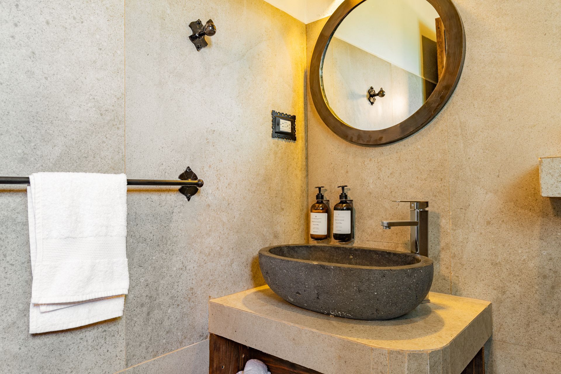 Baño con lavabo de piedra, espejo redondo y toallero.