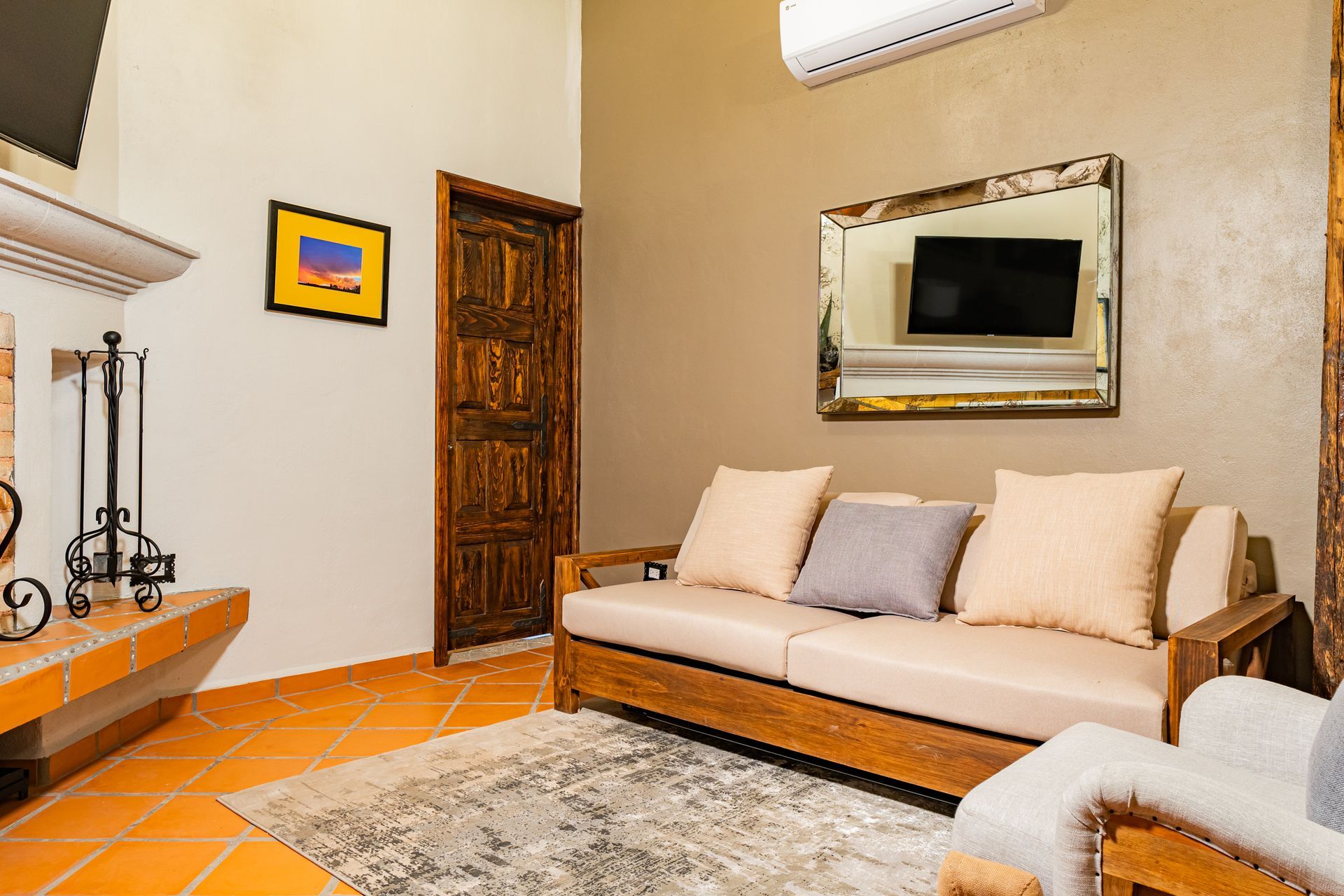 Sala de estar con sofá, alfombra, televisor y chimenea decorativa en una habitación de tonos neutros.