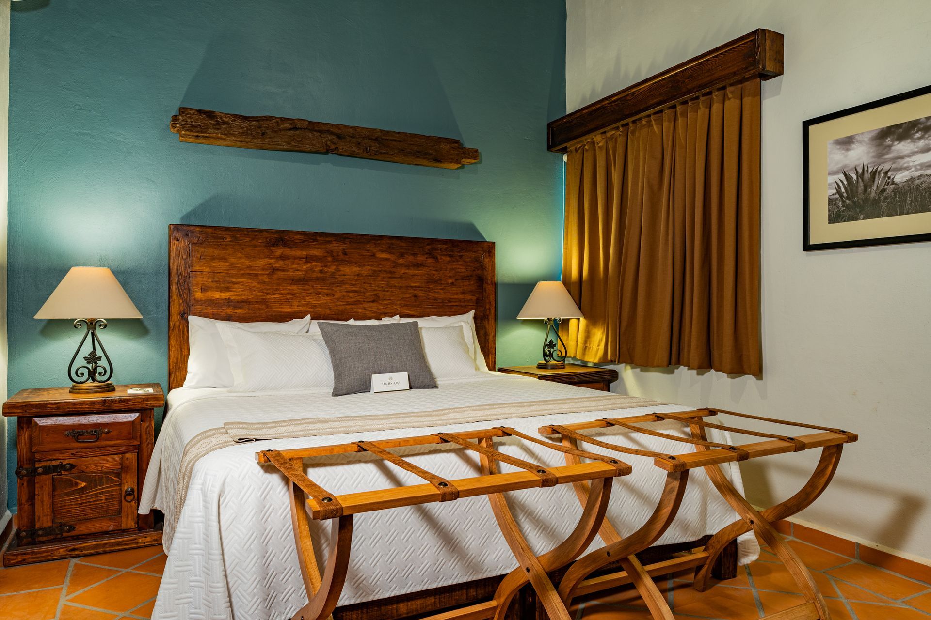 Dormitorio con cama king size, dos mesitas de noche con lámparas, pared azul, cortinas doradas y cuadros enmarcados.