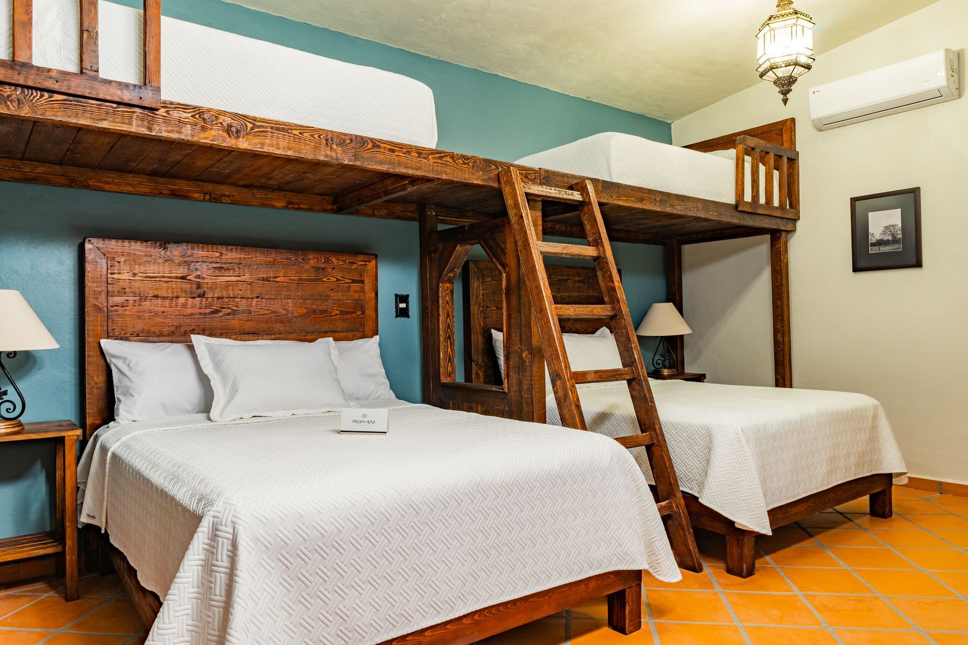 Dormitorio con dos camas individuales y dos camas en altillo; muebles de madera, pared azul, suelo de baldosas naranjas.