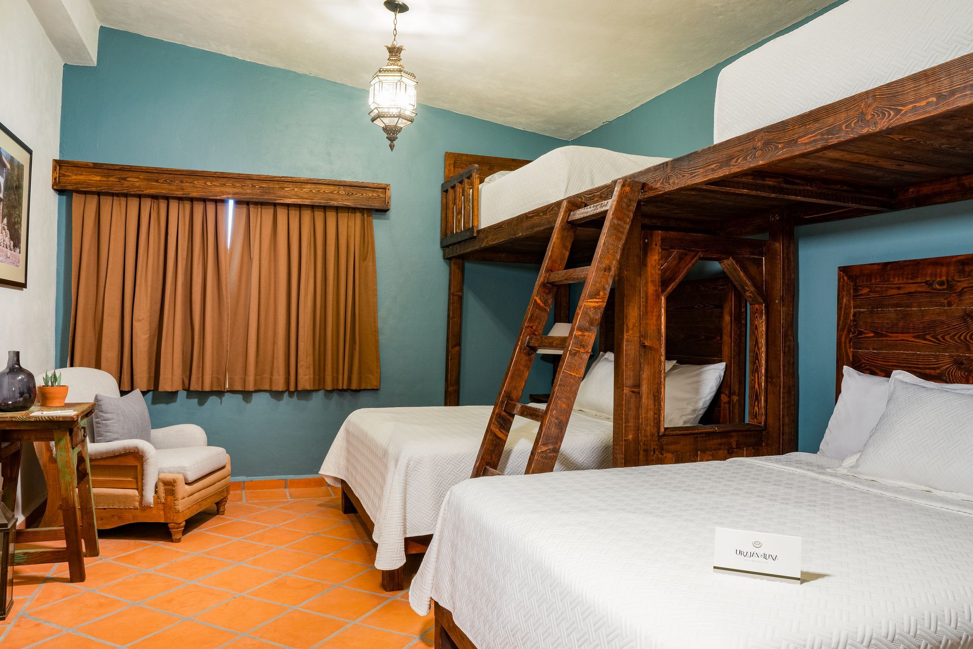 Literas en una habitación con dos camas dobles, cortinas marrones, paredes azules y suelo de terracota.