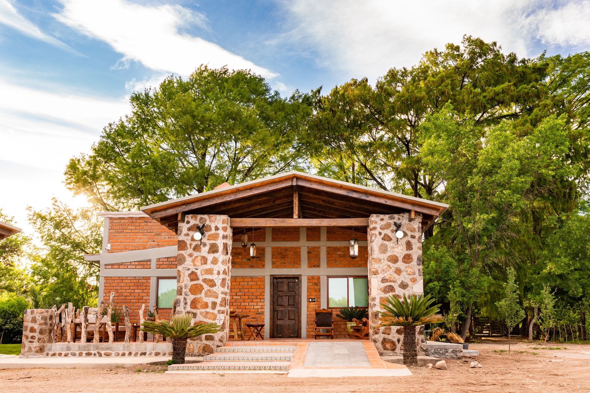 Small brick and stone building with a tiled roof, surrounded by trees and a dirt path.