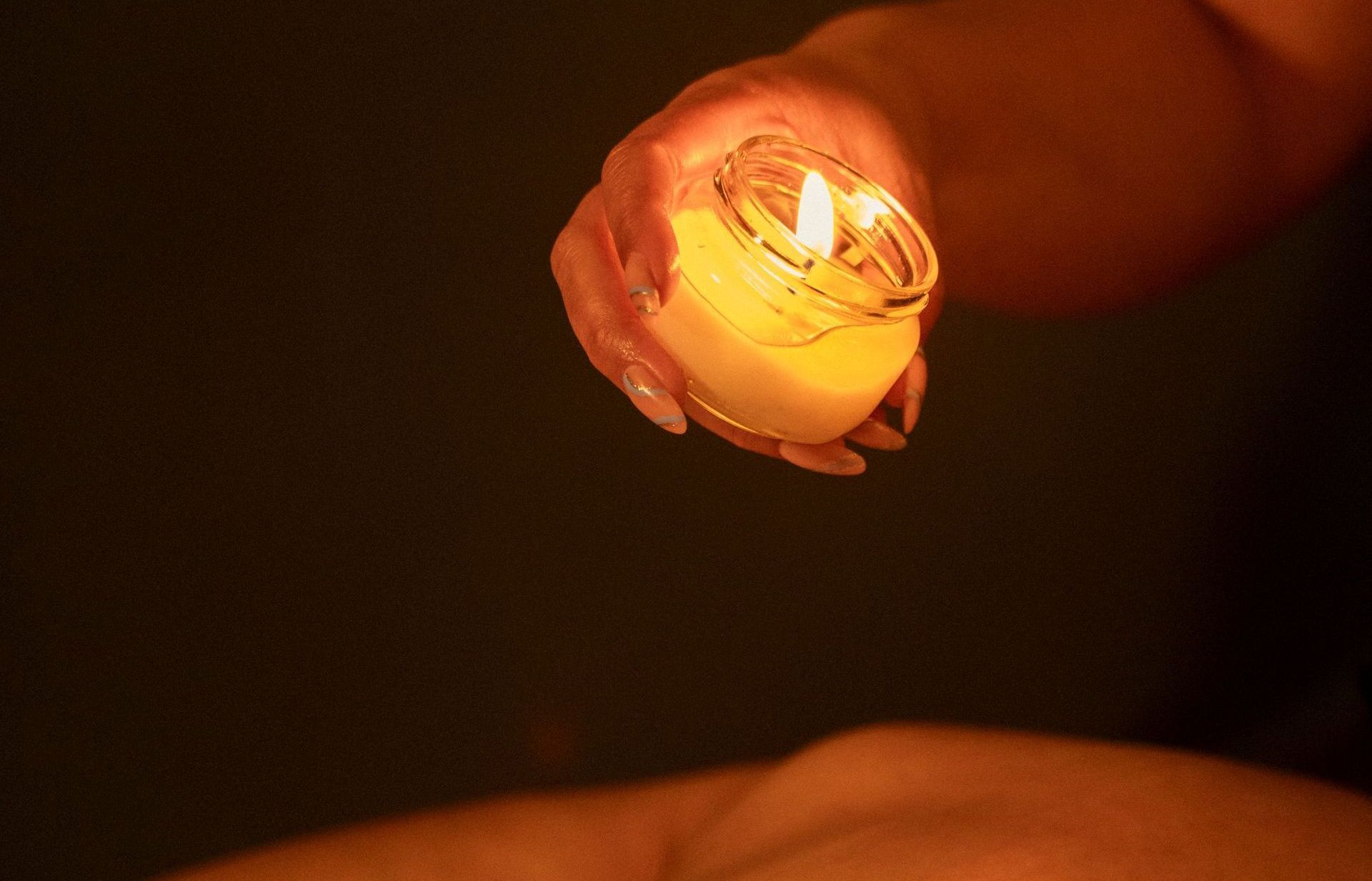 Mano sosteniendo una vela encendida en un frasco de vidrio, que emite un cálido resplandor.