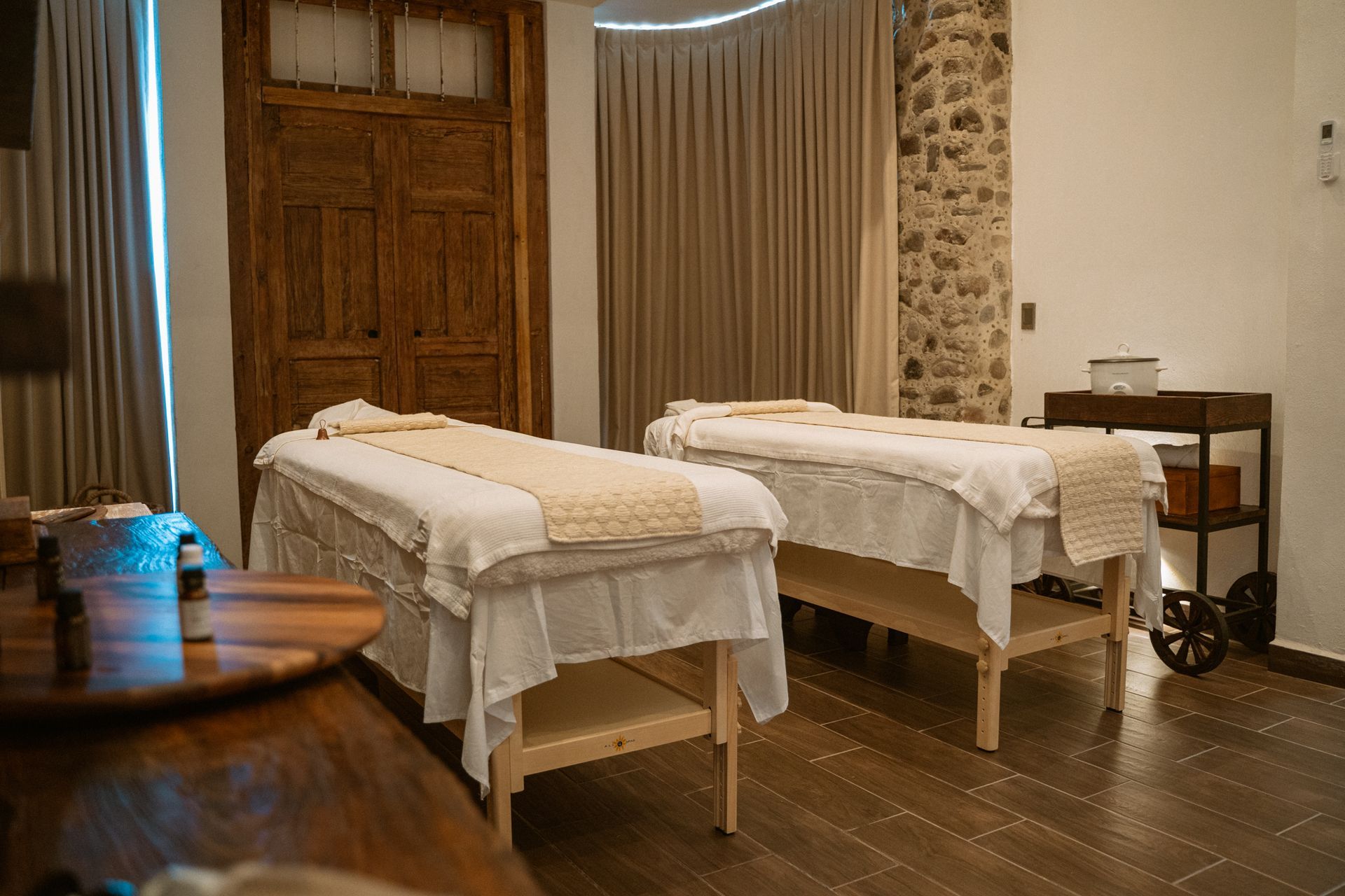 Dos camillas de masaje en una sala de spa, cubiertas con sábanas blancas y caminos de mesa color crema.