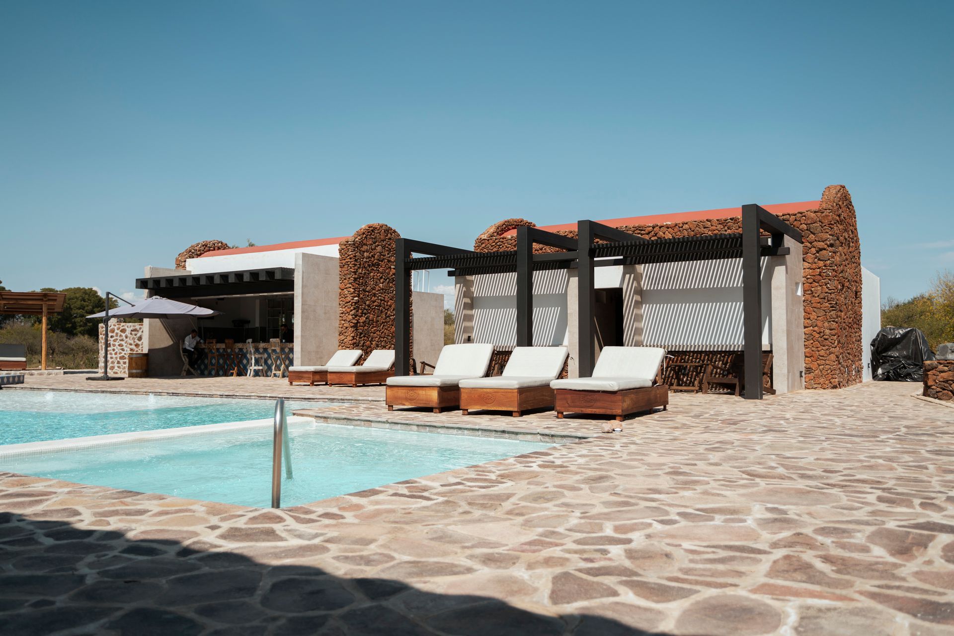 Poolside lounge area with wooden pergolas, sun loungers, and clear blue sky.