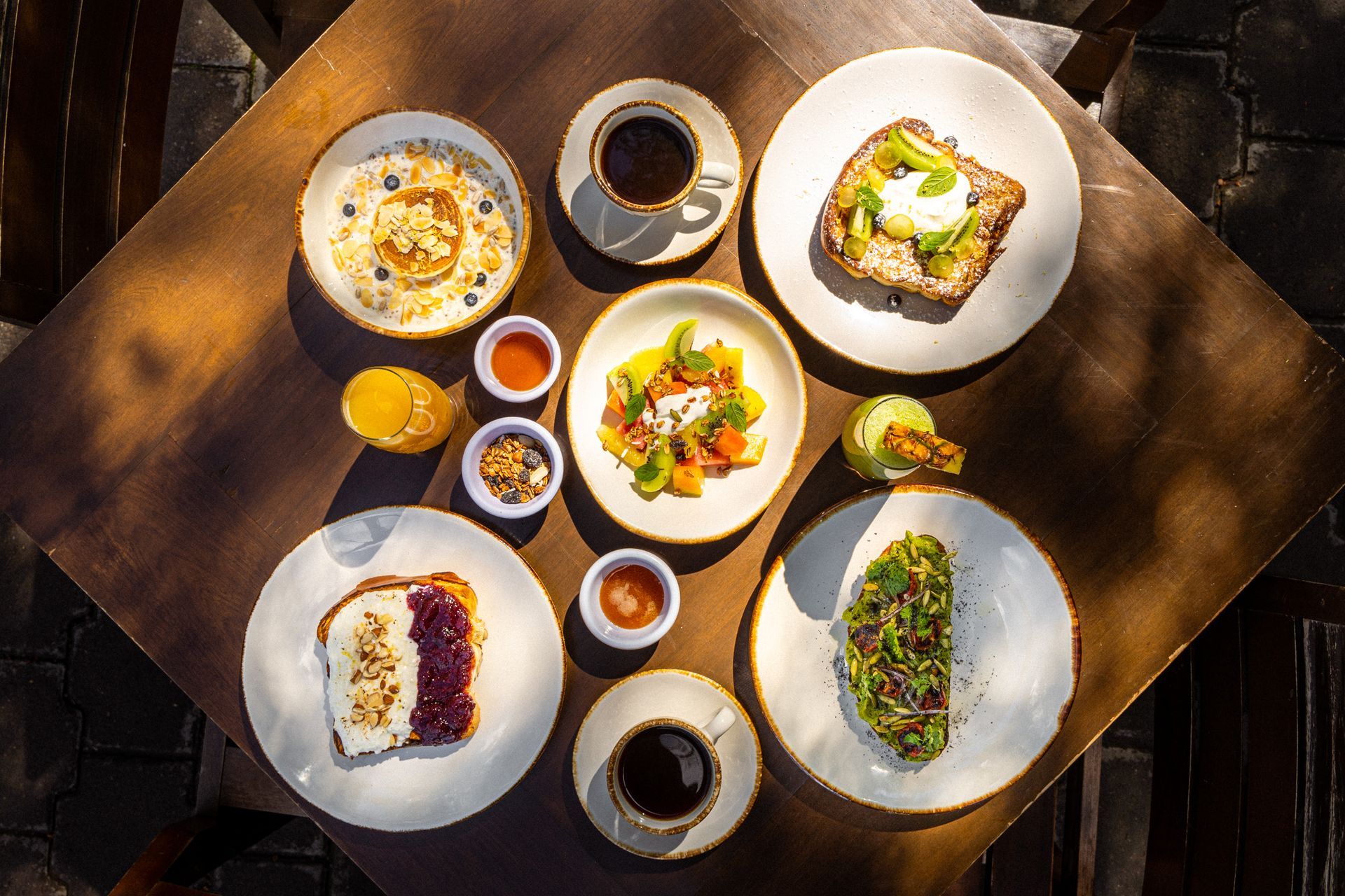 Vista superior de una mesa de madera con varios platos de comida para el desayuno, incluyendo tostadas, avena y café.