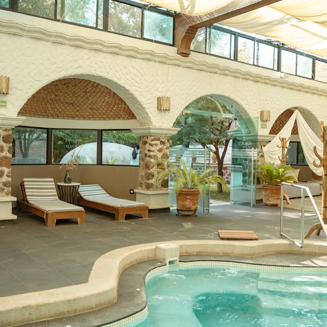 Indoor spa area with pool, arched doorway, chaise lounges, and plants.