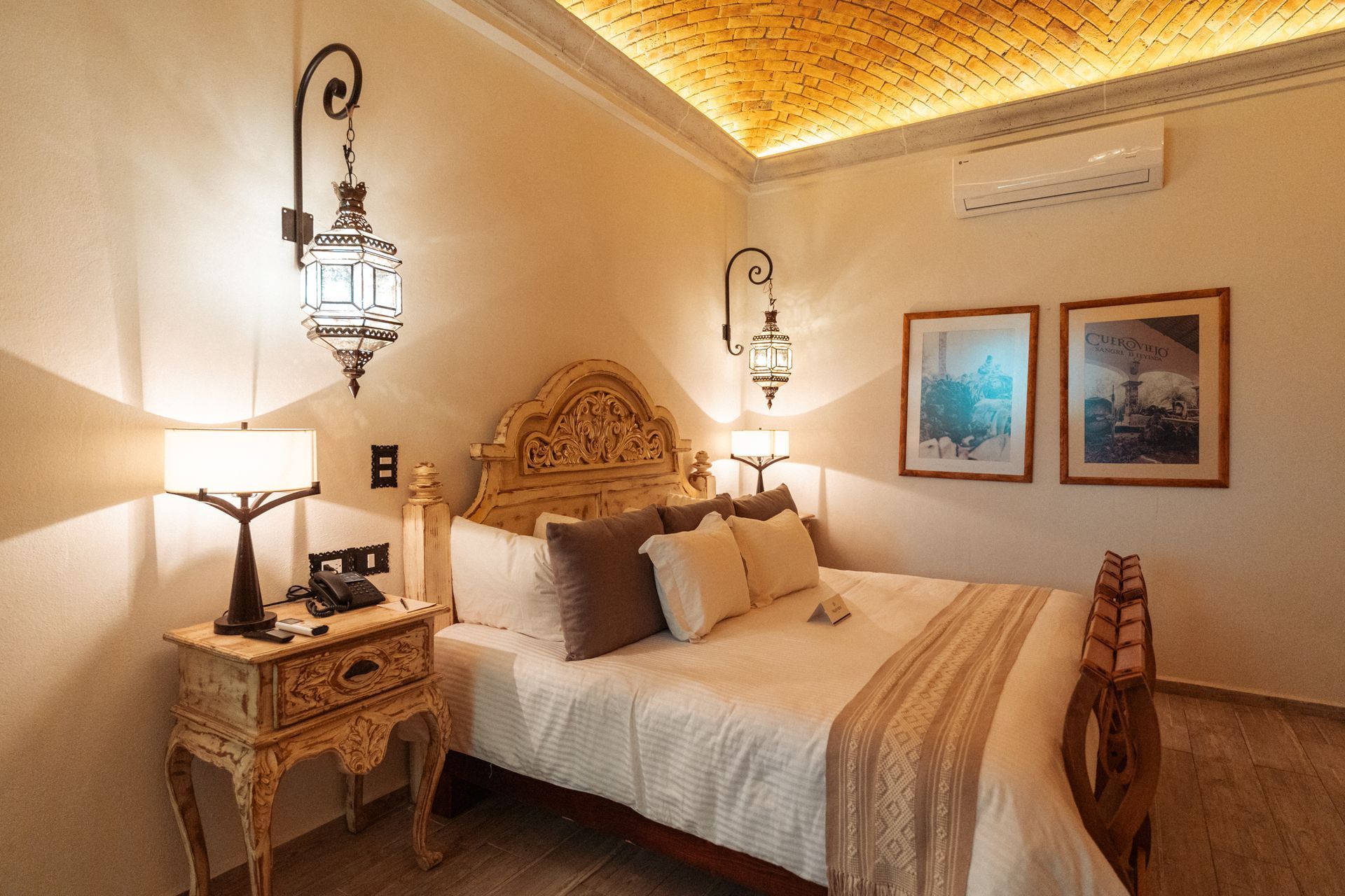 Bedroom with ornate bed, bedside table, hanging lanterns, and two framed pictures.