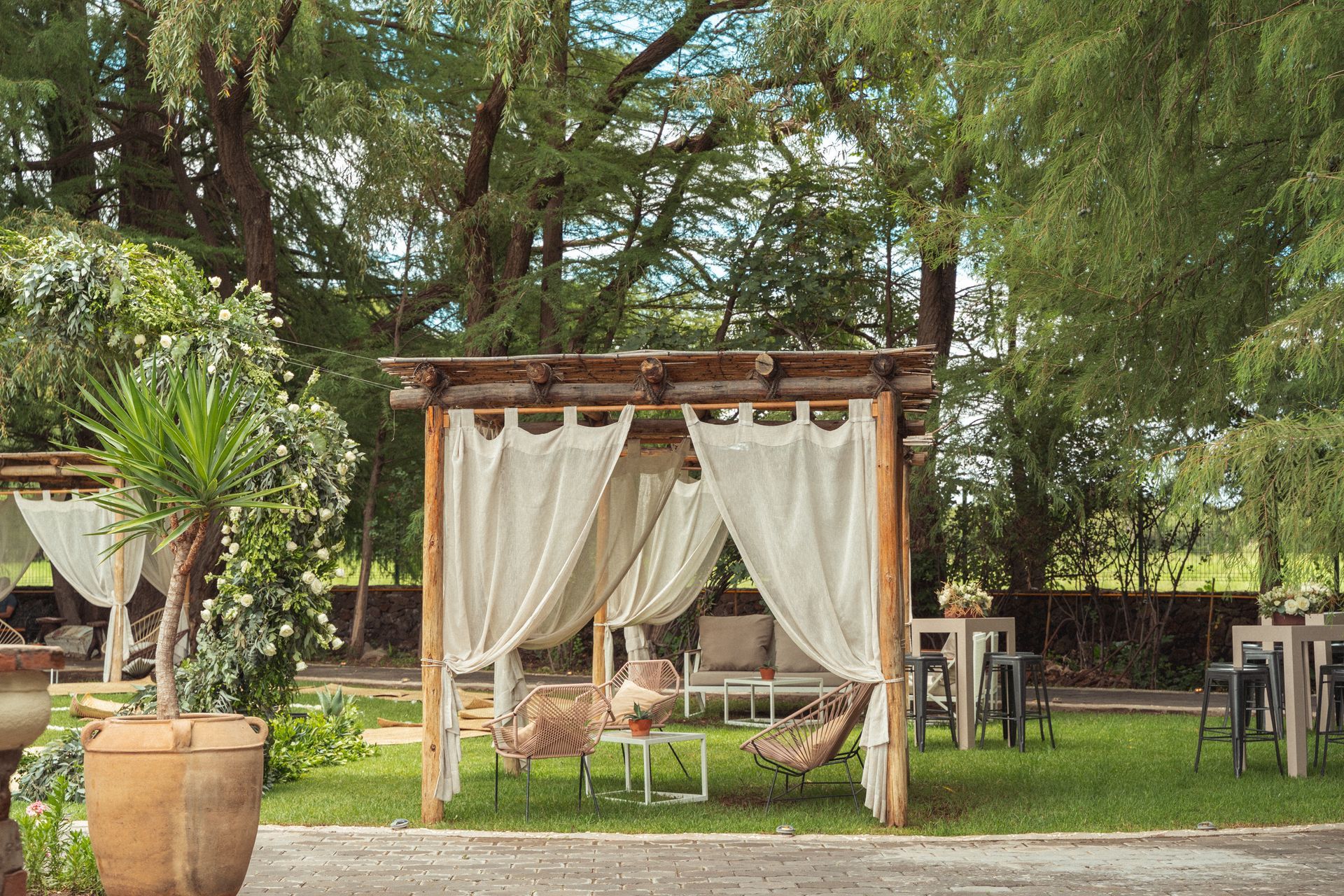 Outdoor seating area with draped cabanas on a grassy lawn. High tables and chairs are nearby.