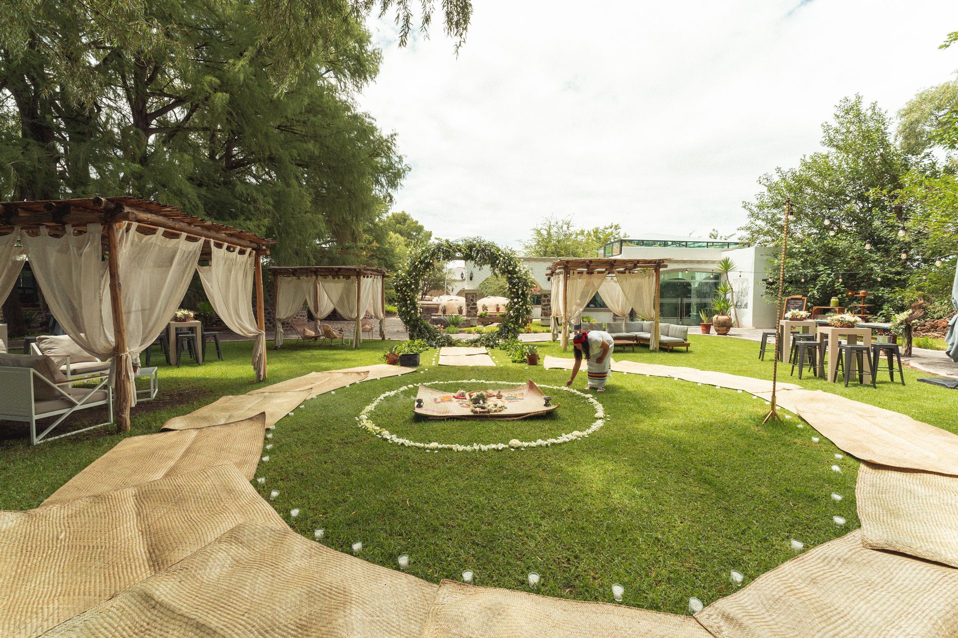 Espacio para eventos al aire libre con glorietas y un arco floral sobre un césped.