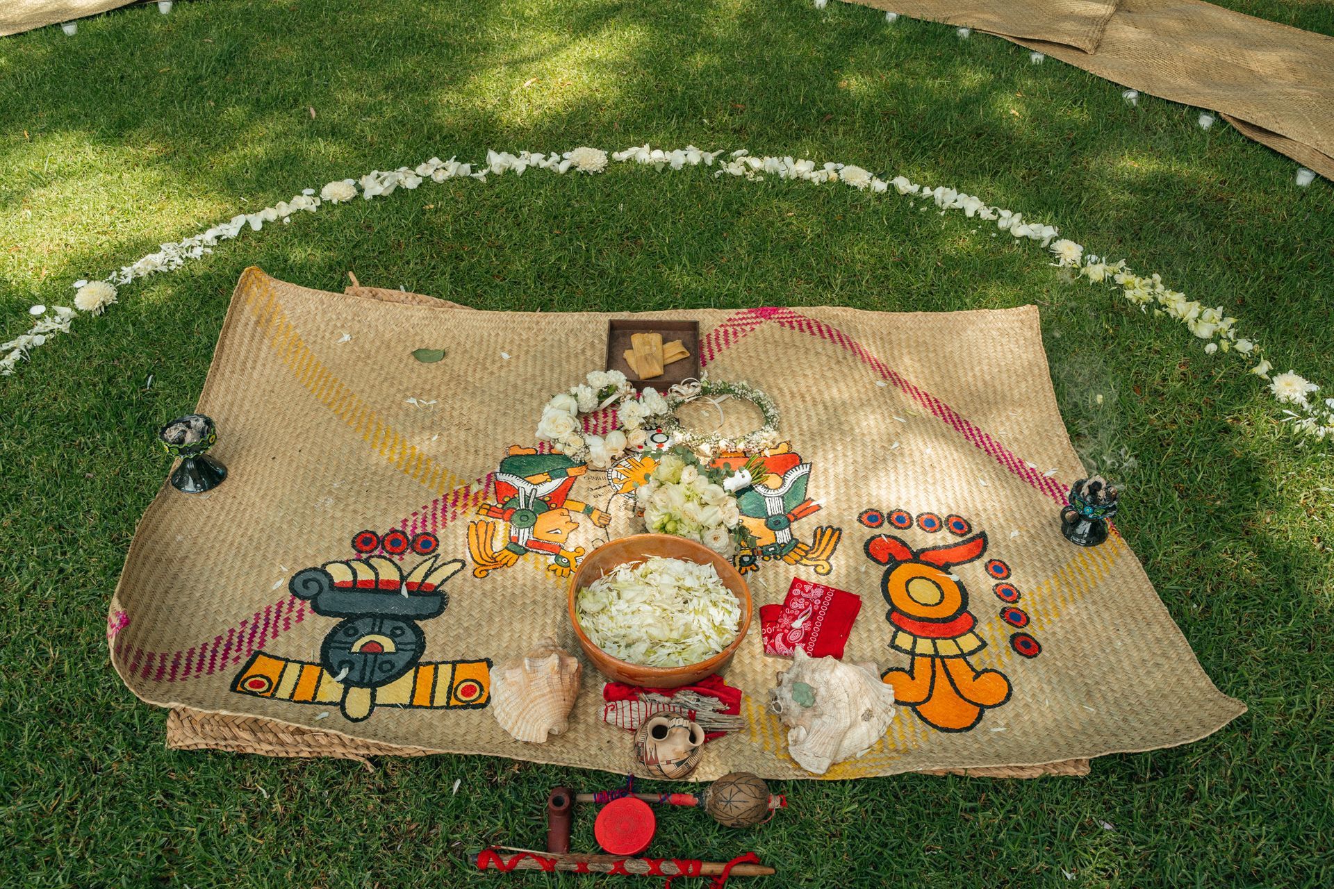 Altar ritual sobre hierba verde, dentro de un círculo de flores blancas.