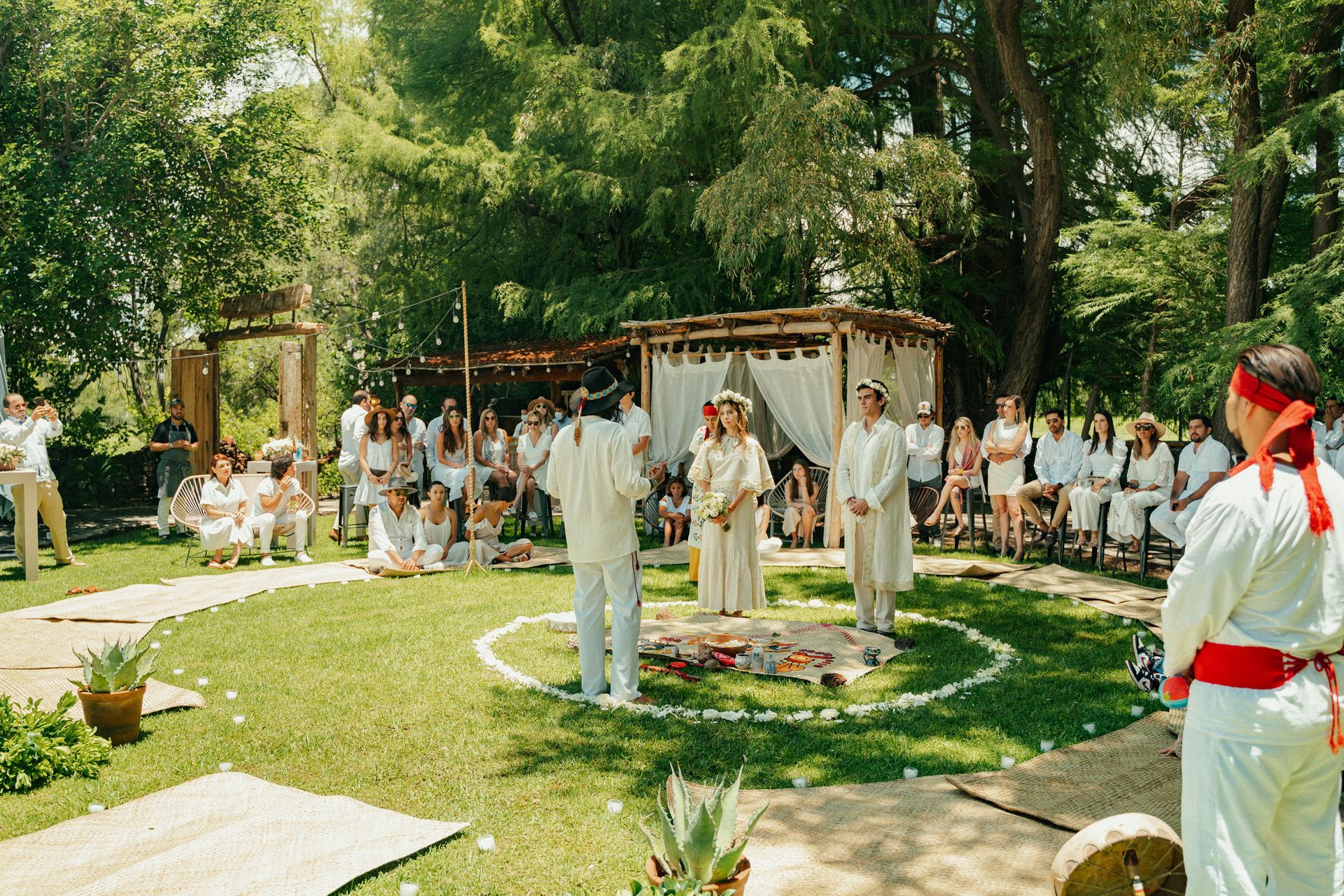 Ceremonia al aire libre con personas vestidas de blanco, una novia y un novio, y un altar circular.