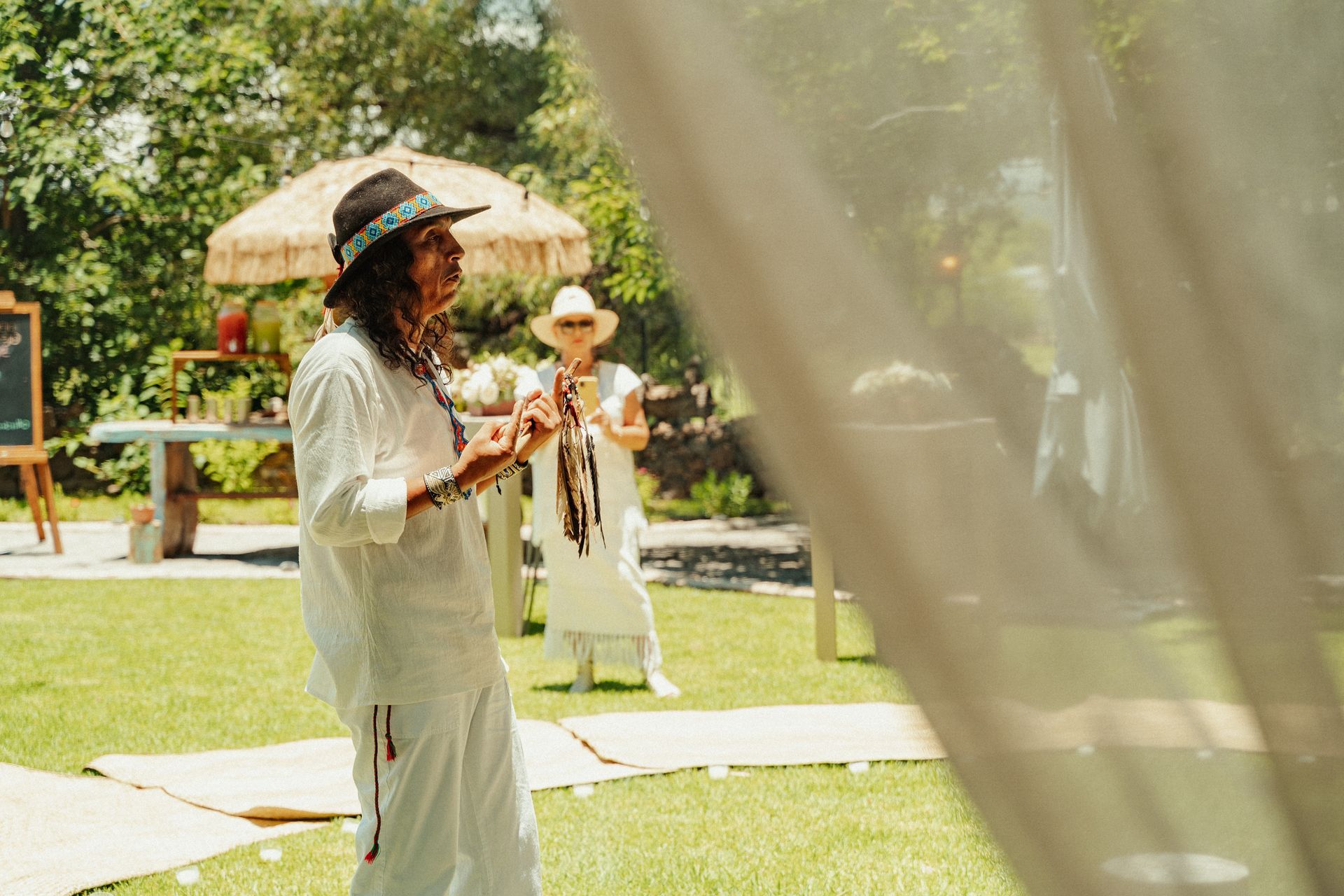 Un hombre vestido de blanco, con sombrero incluido, habla al aire libre; una persona vestida de blanco está detrás de él.