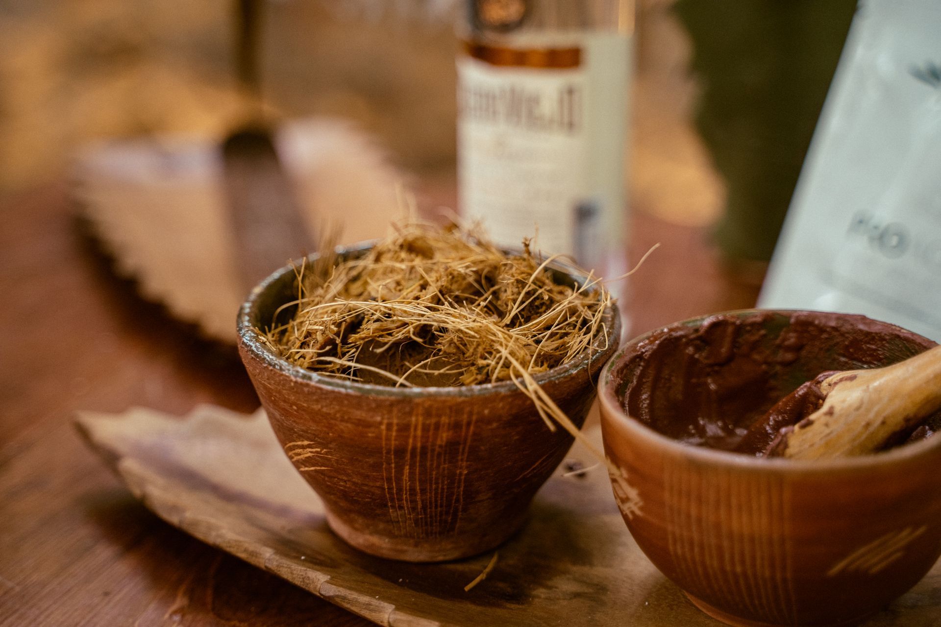Dos pequeños cuencos de madera, uno con fibras vegetales secas y el otro con una pasta marrón.