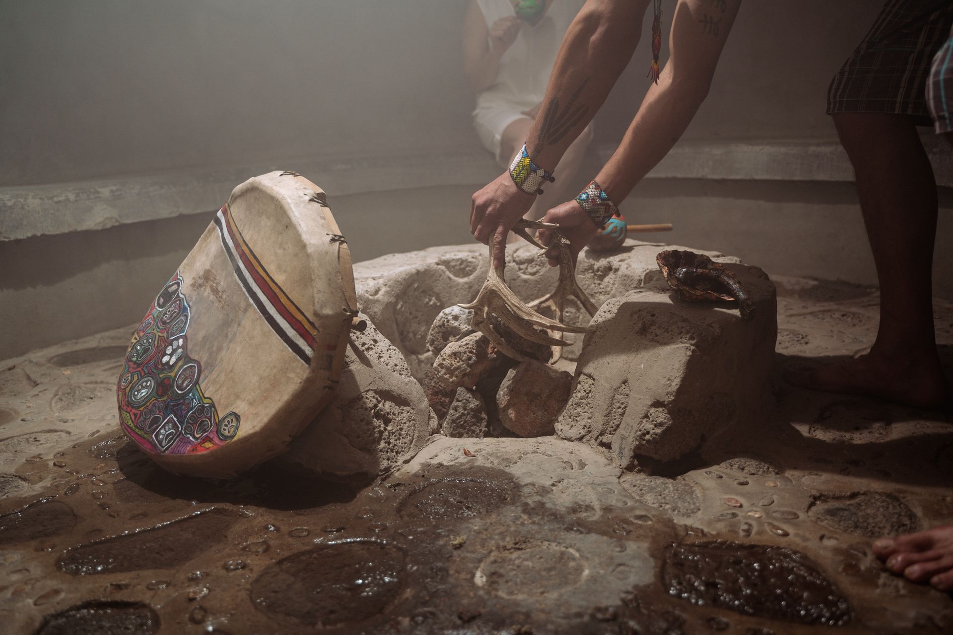Unas manos vierten agua sobre piedras calientes en un espacio tenuemente iluminado y lleno de vapor. 