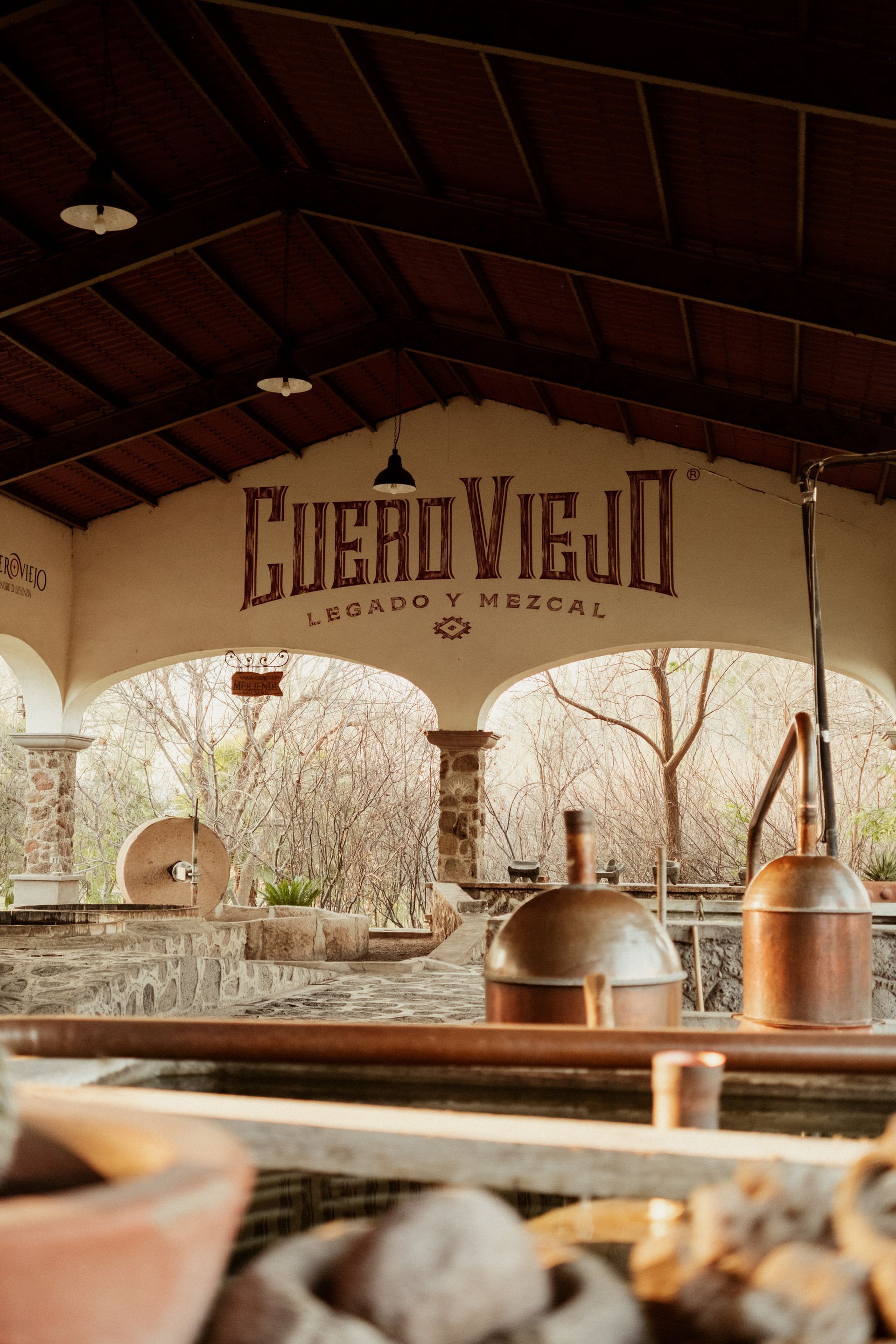 Destilería de mezcal Cuero Viejo con alambiques de cobre, letrero rústico y ambiente al aire libre.