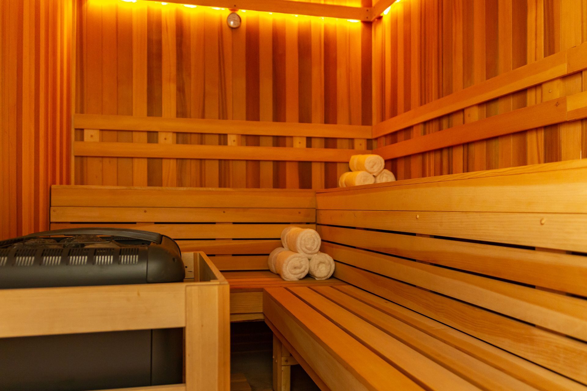 Interior de sauna de madera con bancos, toallas enrolladas y calefactor.