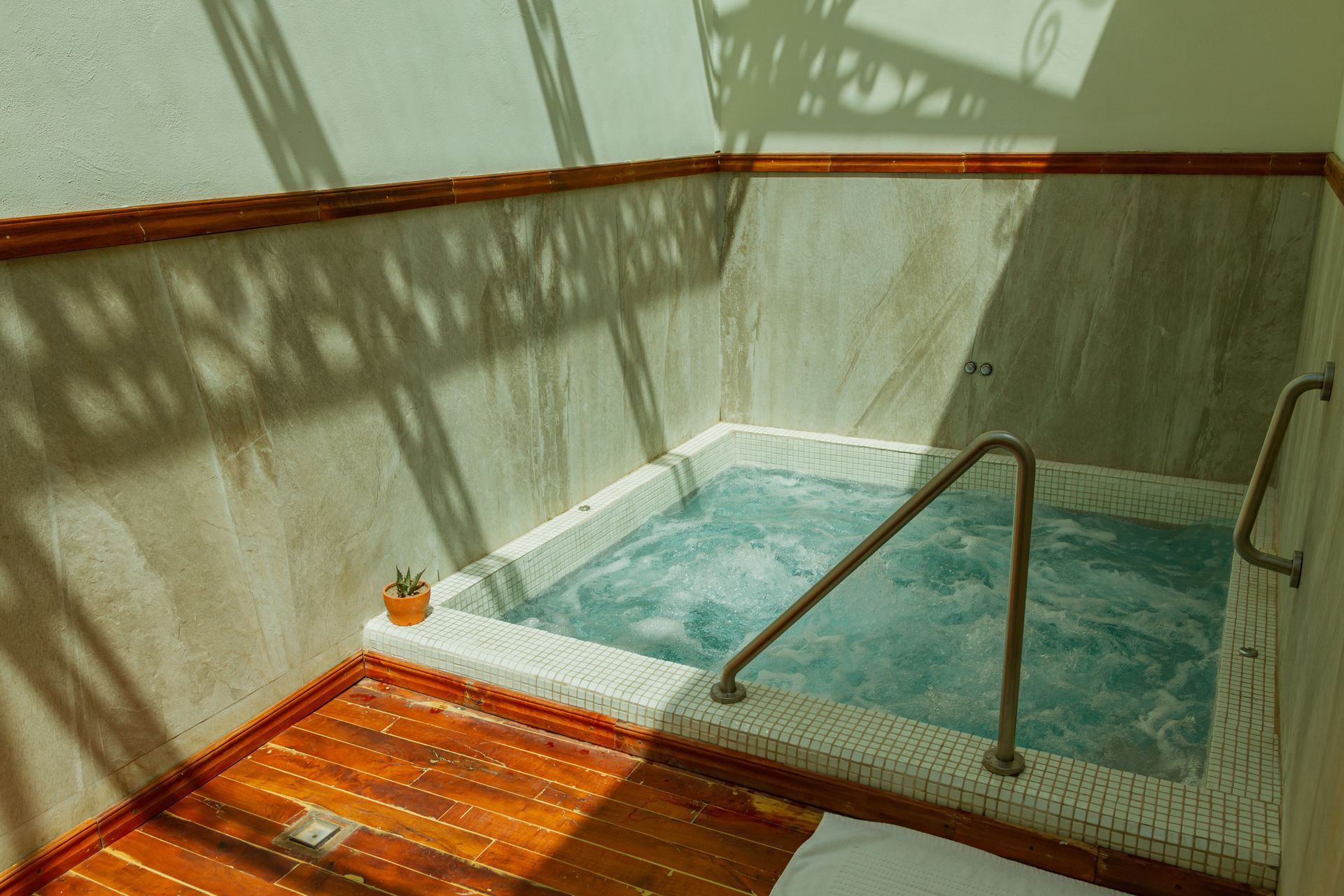 Pequeño jacuzzi interior con agua burbujeante, suelo de madera y barandilla.