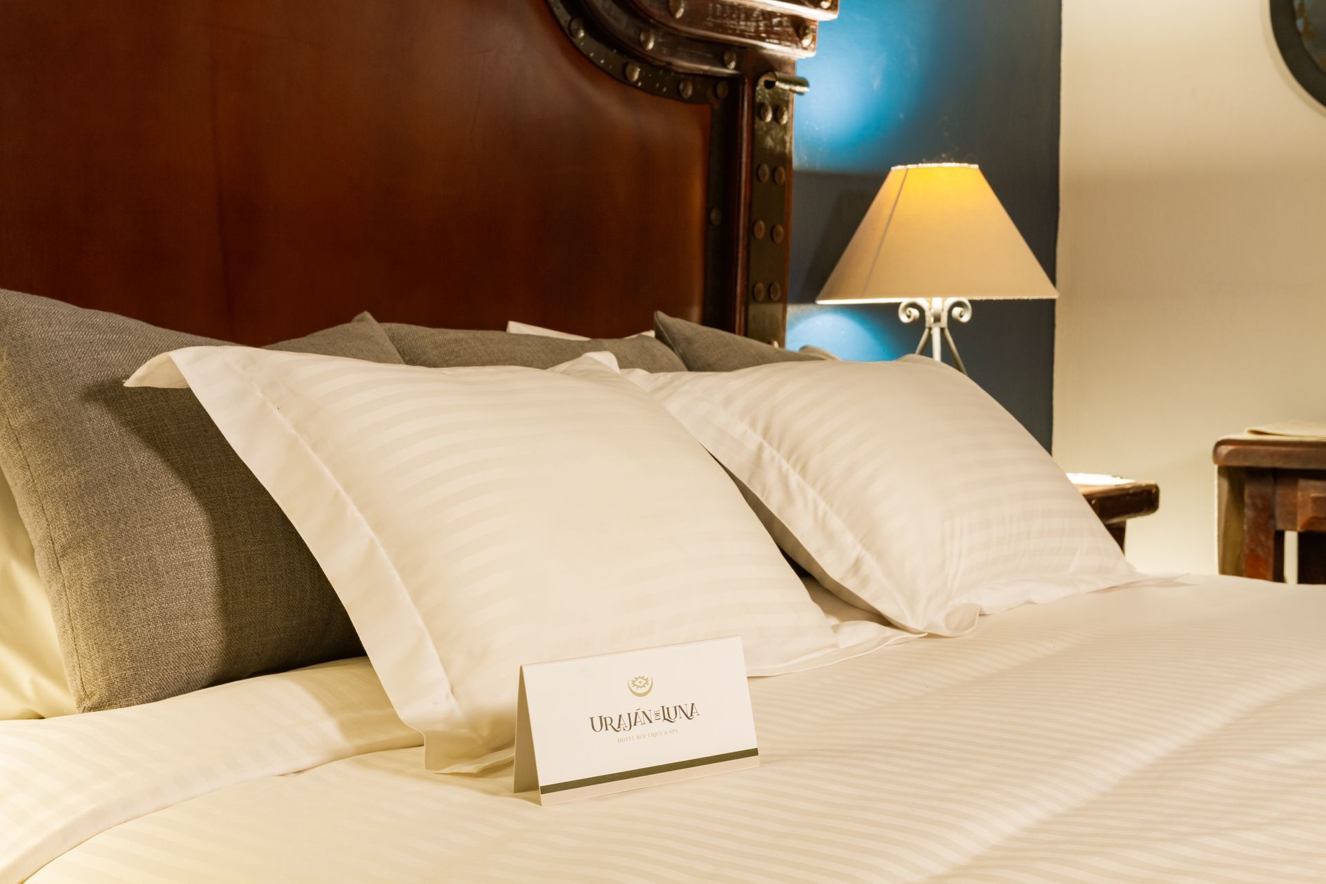 Bed with white linens and pillows, dark wood headboard, lamp, and a sign.