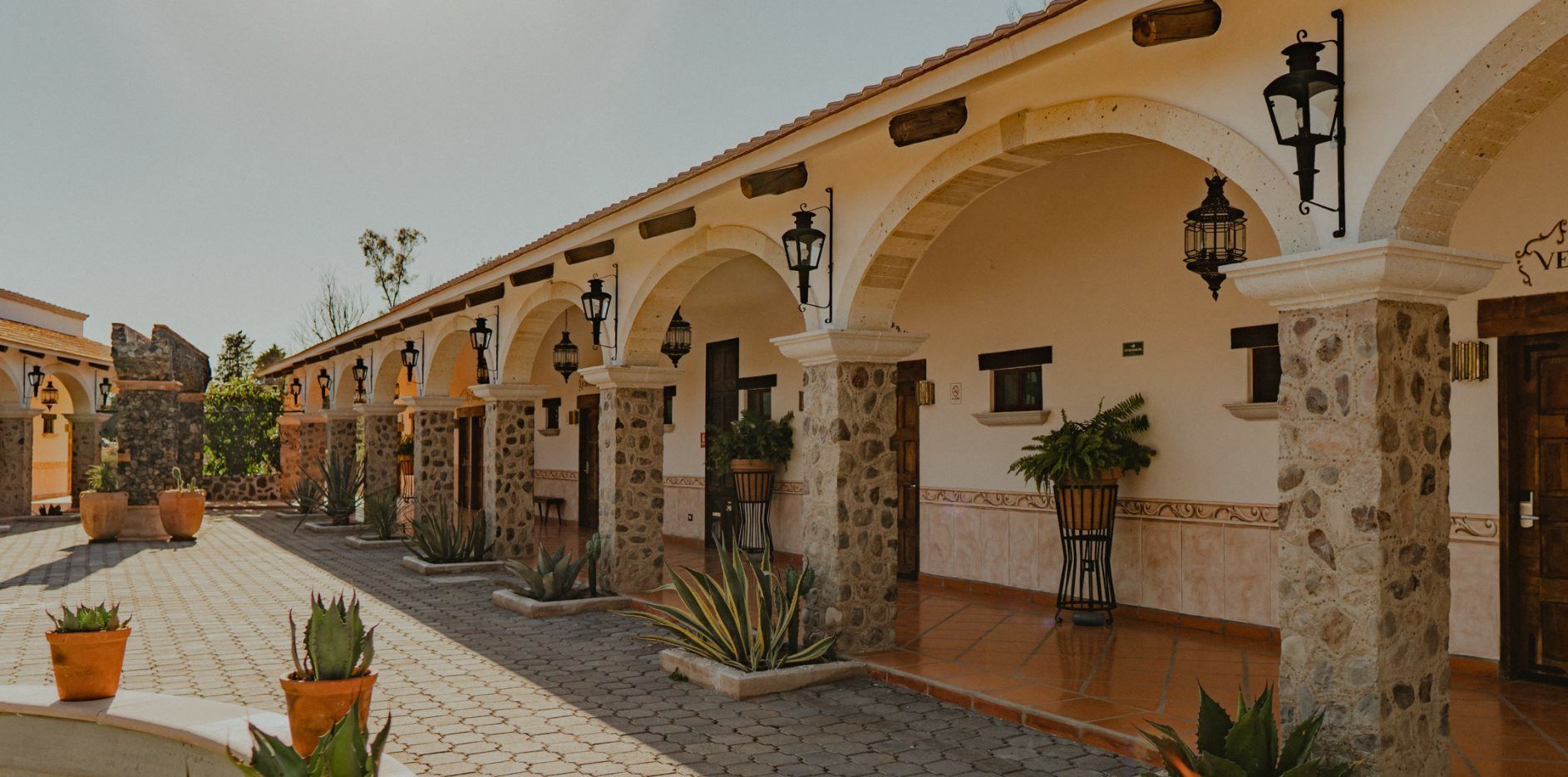 Courtyard with arched walkway, stone columns, terracotta pots, plants, and lanterns.