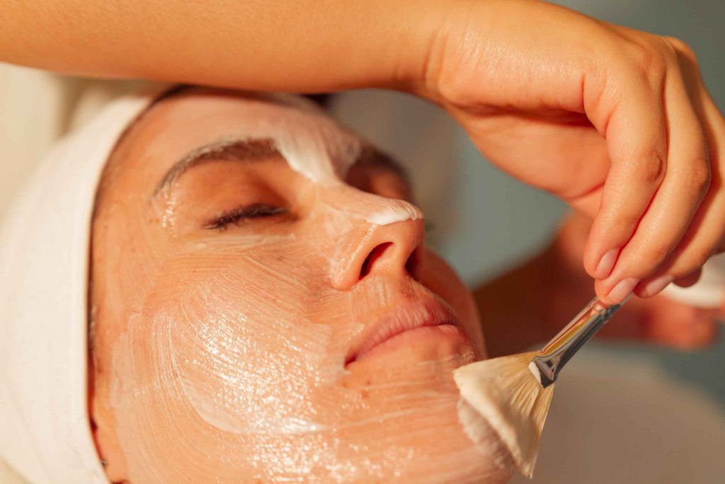 Persona recibiendo tratamiento facial; crema aplicada en el rostro con una brocha.