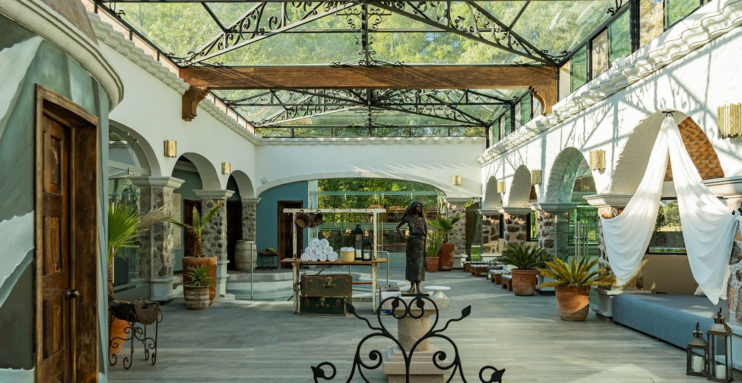 Elegante patio cerrado con techo de cristal. Arcos, plantas, estatuas y zonas de estar.