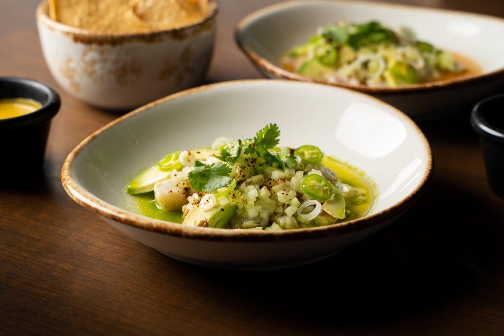 Three bowls of ceviche topped with herbs and jalapeños, alongside a bowl of chips and dipping sauce.