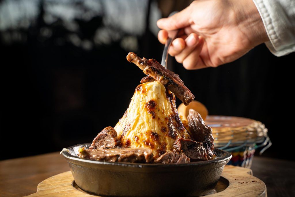 A person using a fork to lift a piece of meat from a dish piled with mashed potatoes and steak.