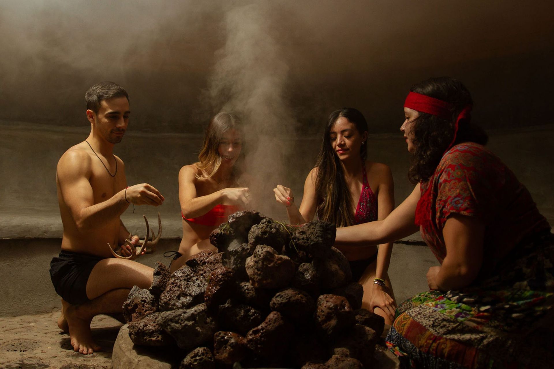 Four people in a dimly lit cave gather around a smoking pile of rocks.