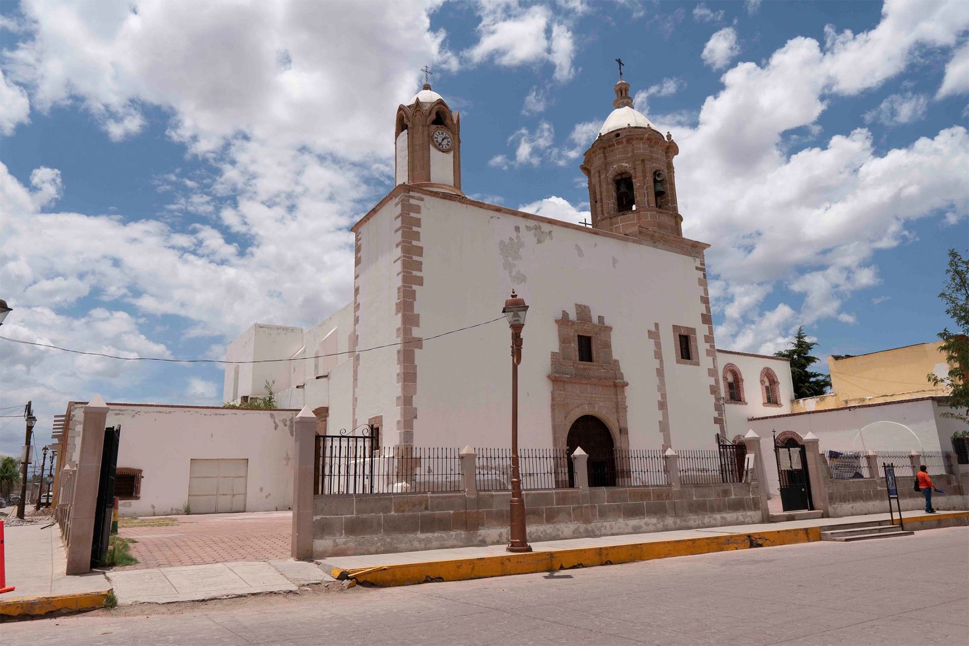 White church with two bell towers, pink trim, and arched entrance under a partly cloudy sky.