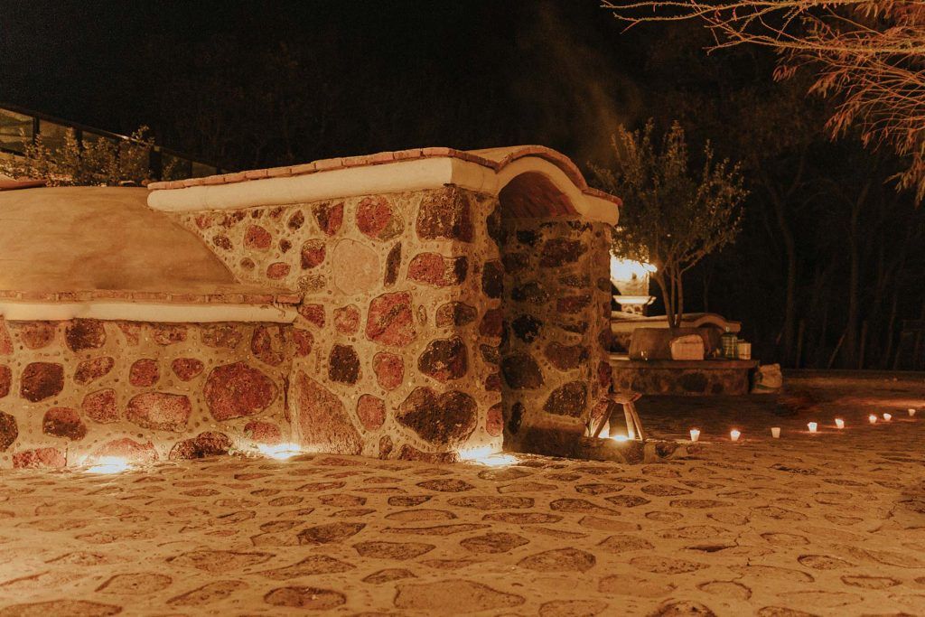 Stone building exterior at night, lit by small candles, dark background with trees.