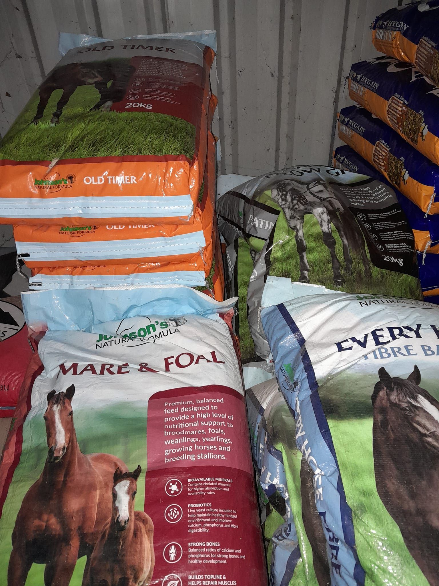 Stacked bags of horse feed in a storage area, some labeled