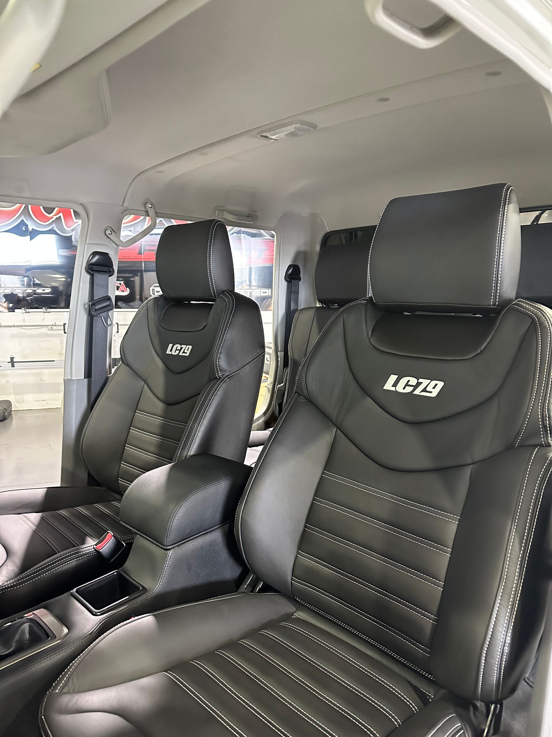 Two black leather racing seats inside a van, with white stitching and embroidered logos.  — Outback Auto NT in Berrimah, NT
