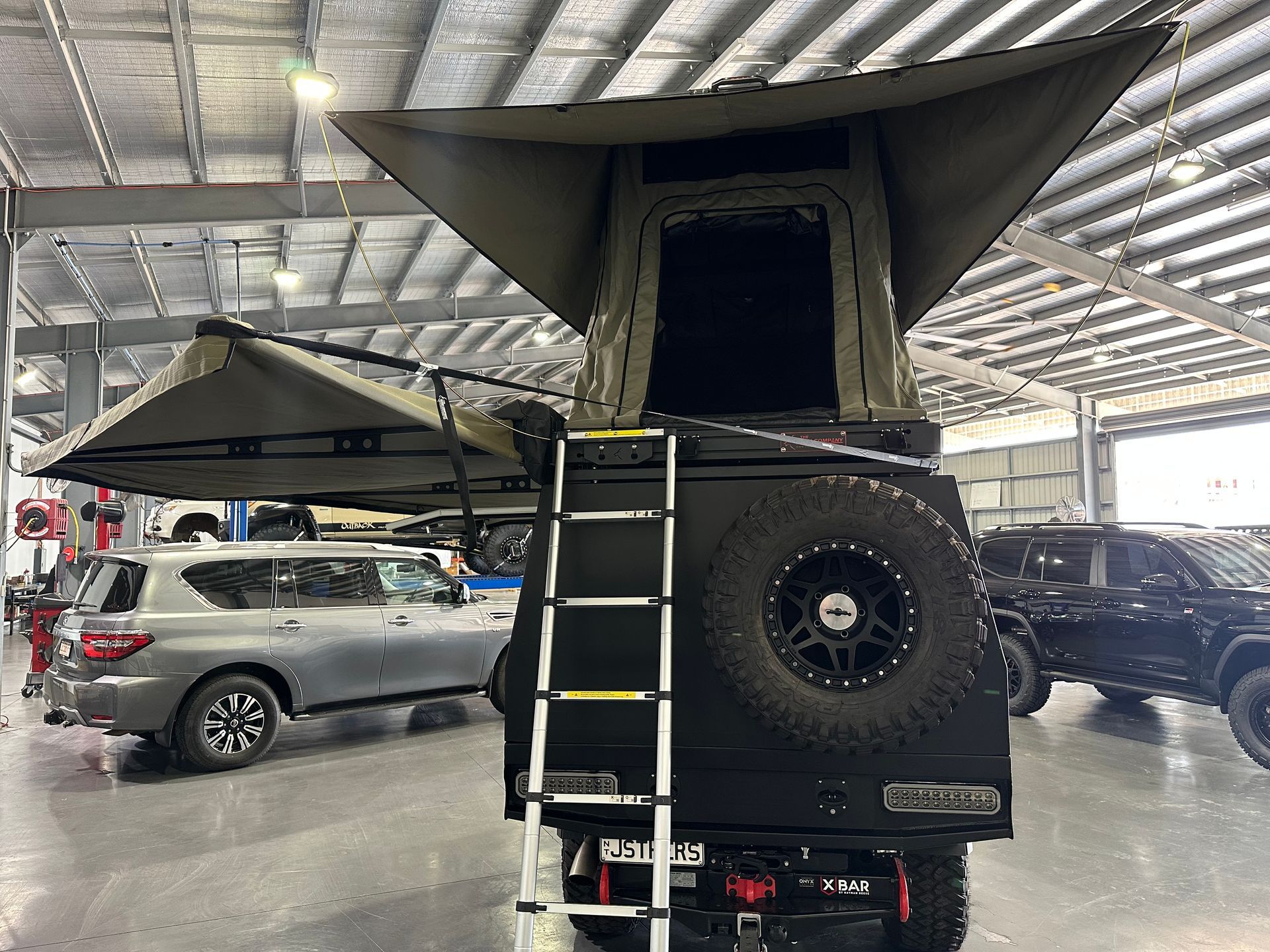 Off-road camper truck with rooftop tent and ladder parked indoors under a metal roof  — Outback Auto NT in Berrimah, NT