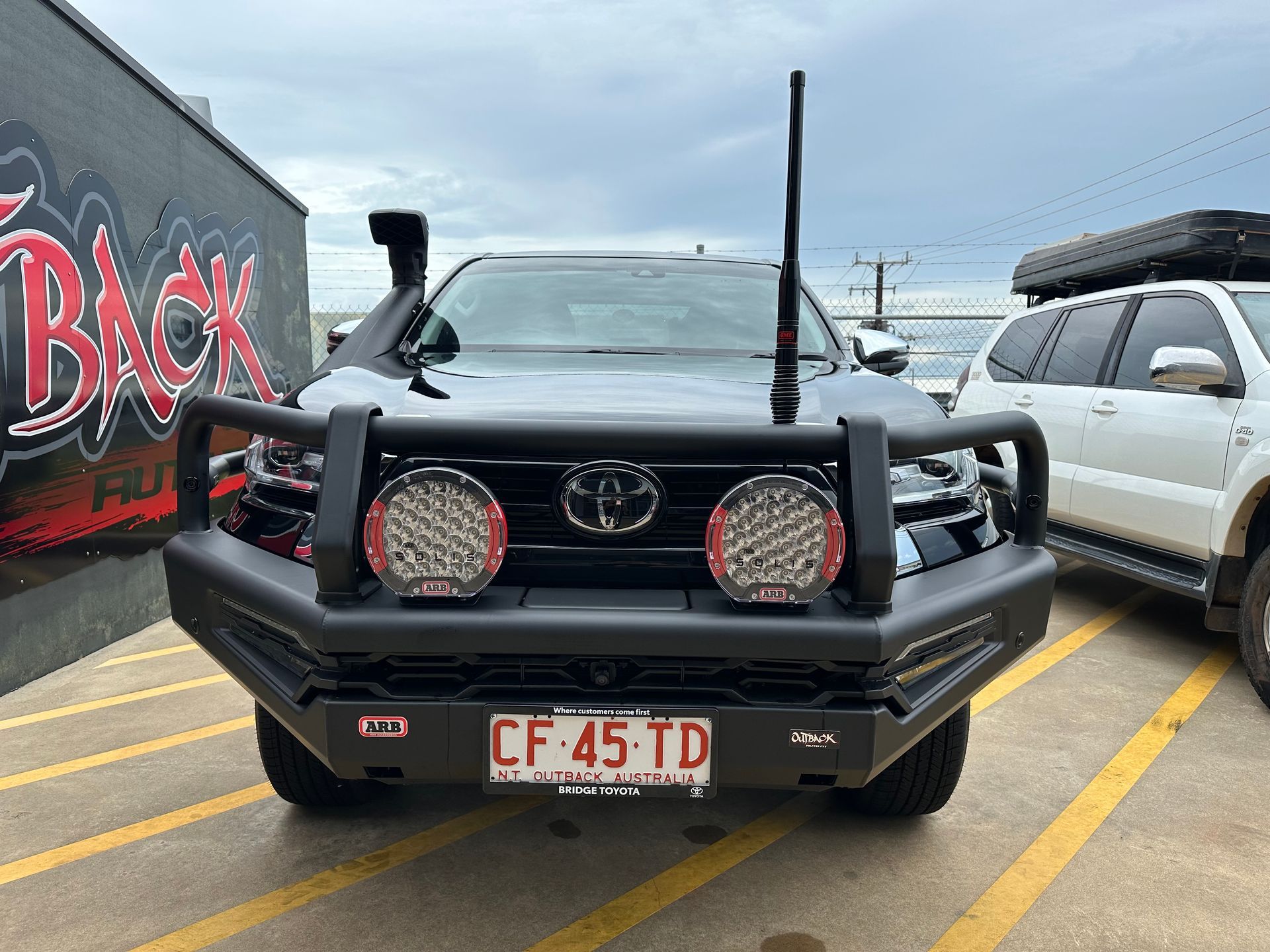 Black Toyota SUV parked in a lot, viewed from the front with off-road gear and red accent lights.  — Outback Auto NT in Berrimah, NT