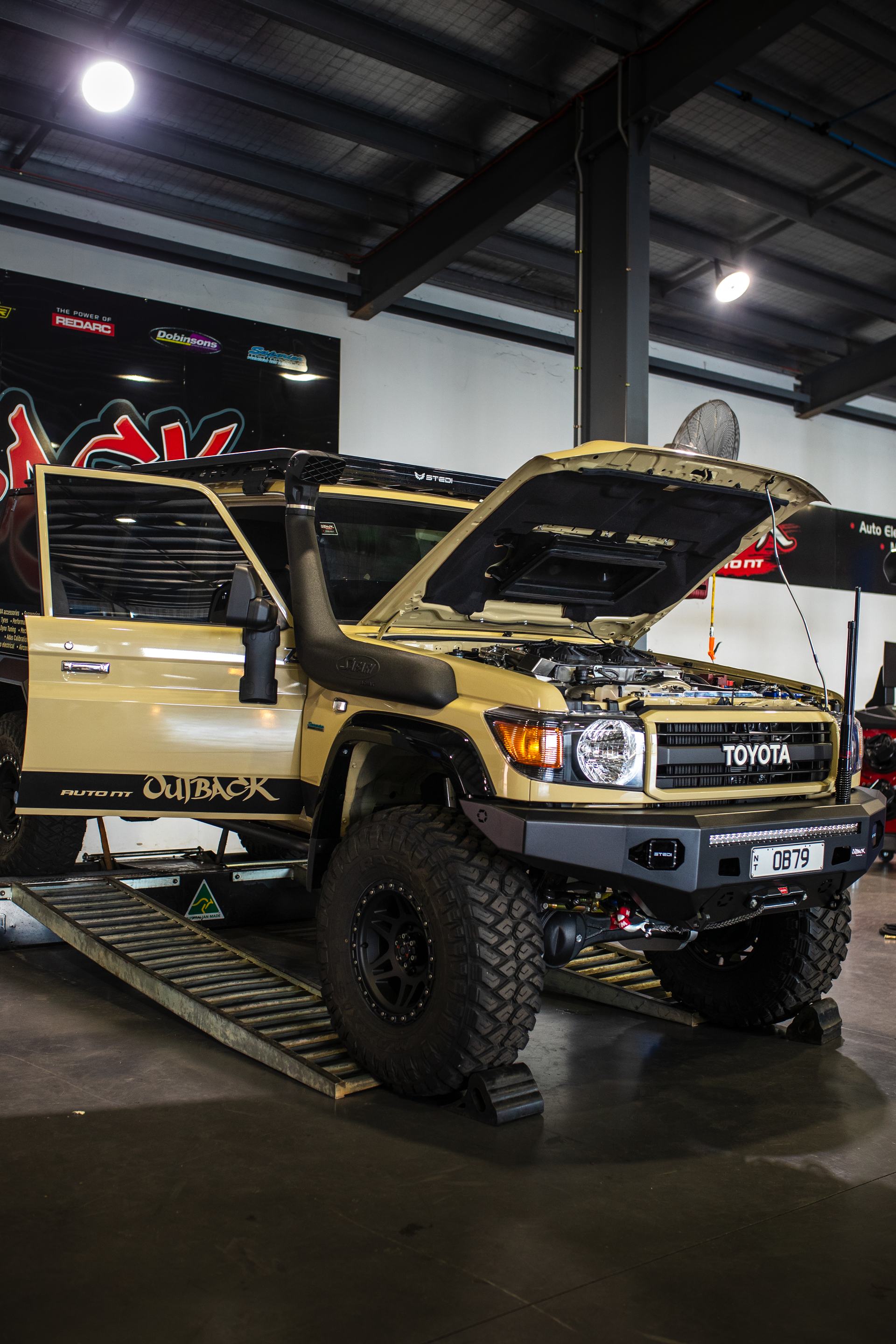 Modified yellow off-road truck with open hood and doors displayed indoors at an auto show  — Outback Auto NT in Berrimah, NT