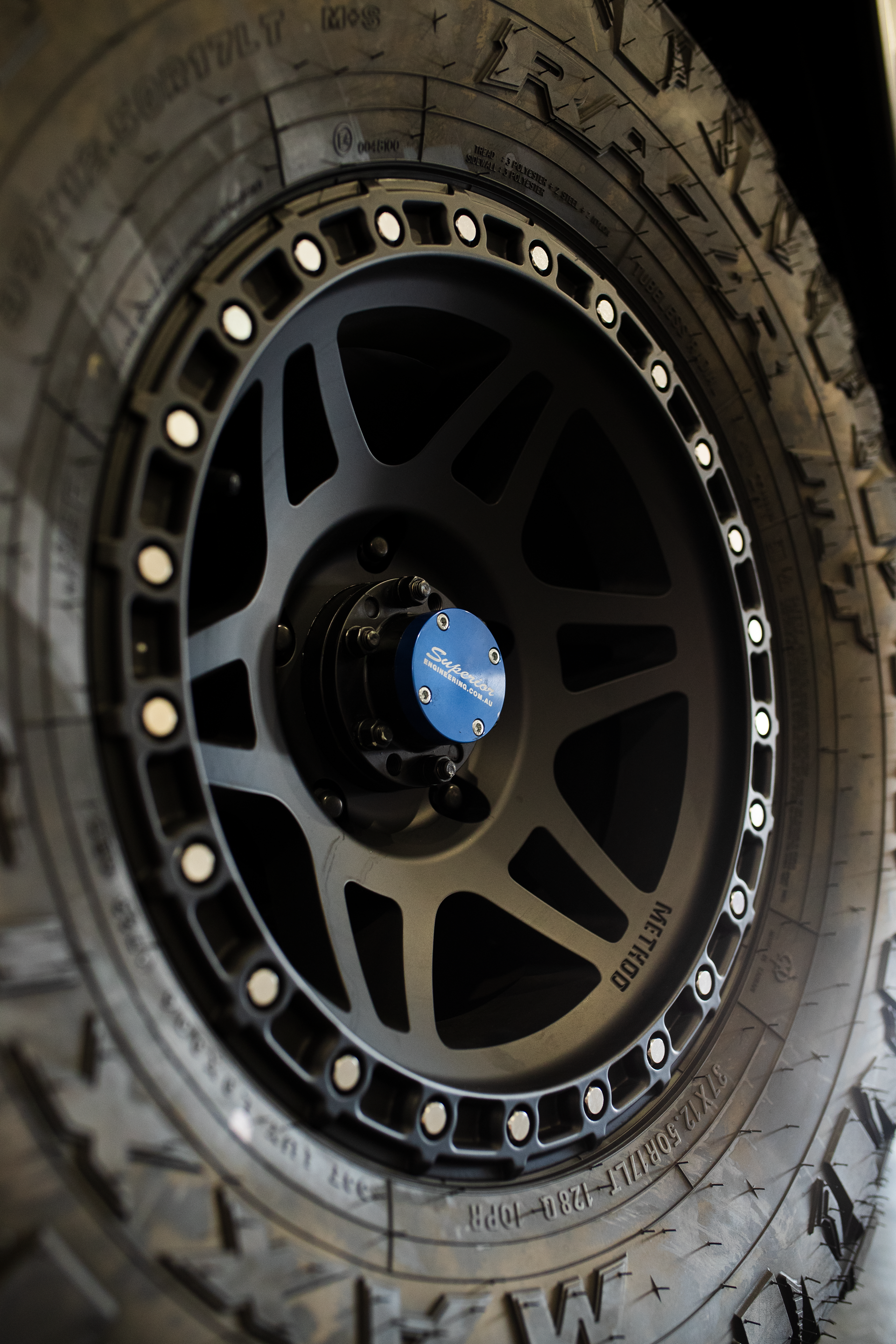 Black off-road tire on a matte black alloy wheel with blue center cap and silver bolt ring — Outback Auto NT in Berrimah, NT