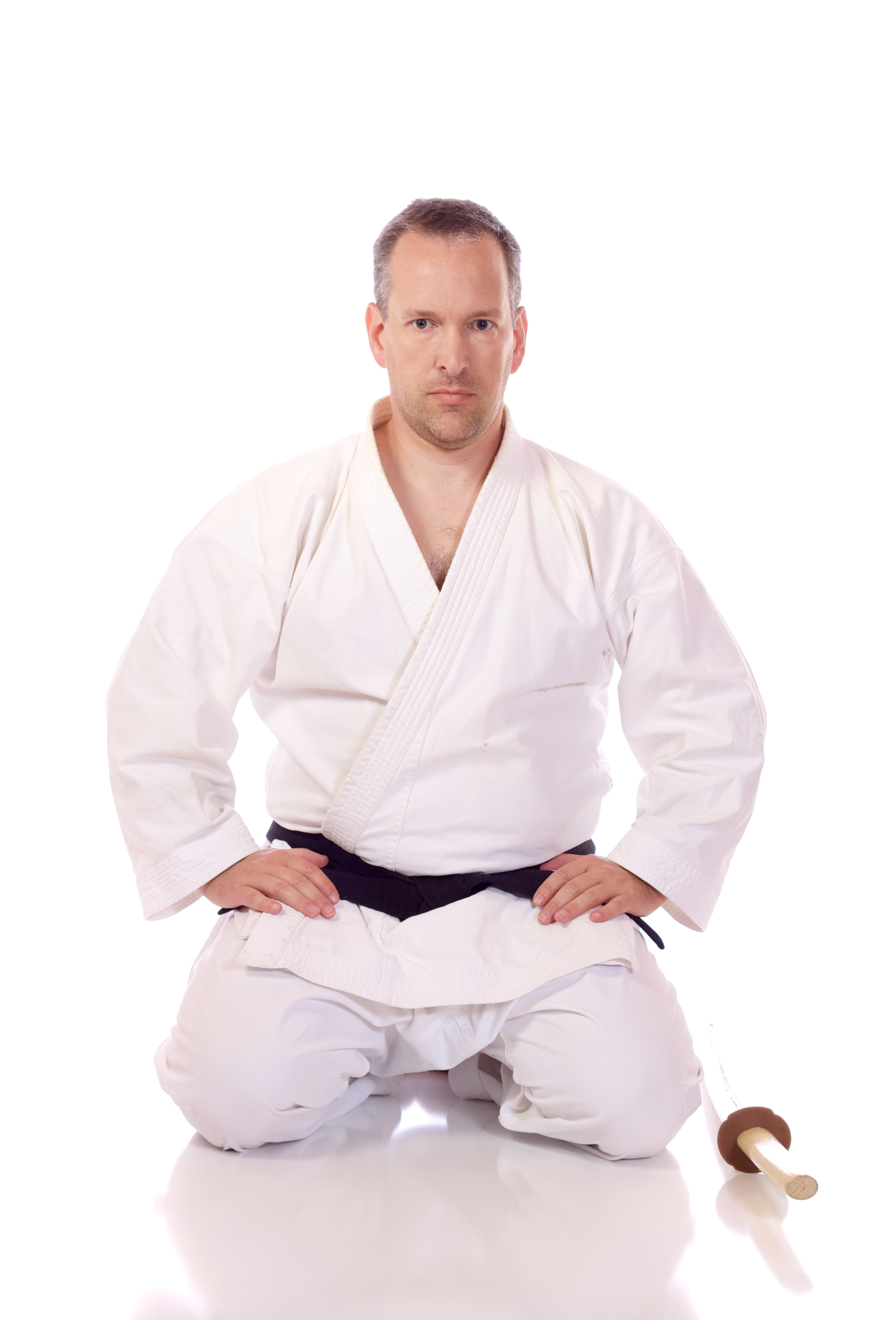 A man in a karate uniform is kneeling down with his hands on his hips.